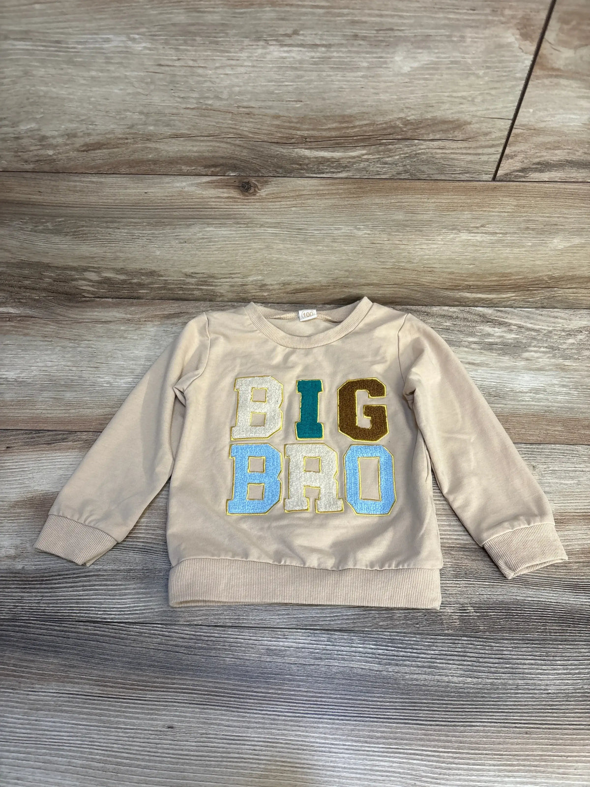Beige toddler sweatshirt with colorful BIG BRO letters on wood background, kids clothing