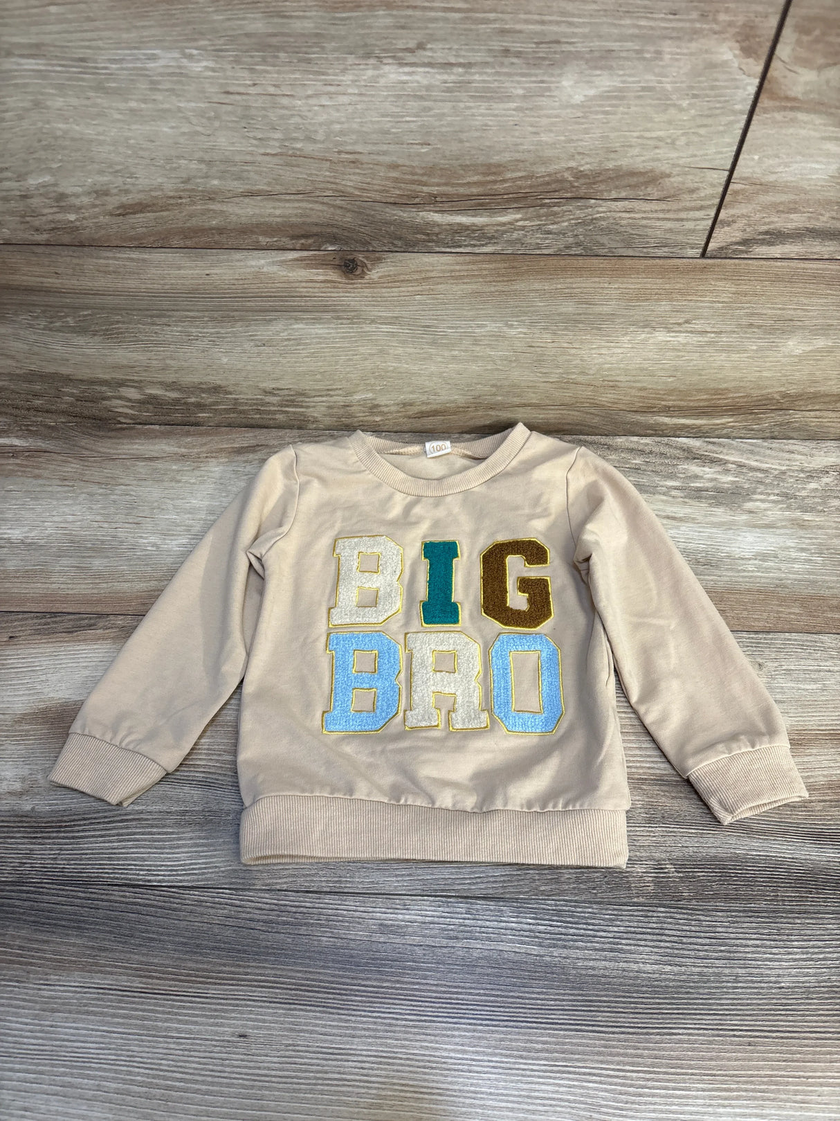 Beige toddler sweatshirt with colorful BIG BRO letters on wood background, kids clothing
