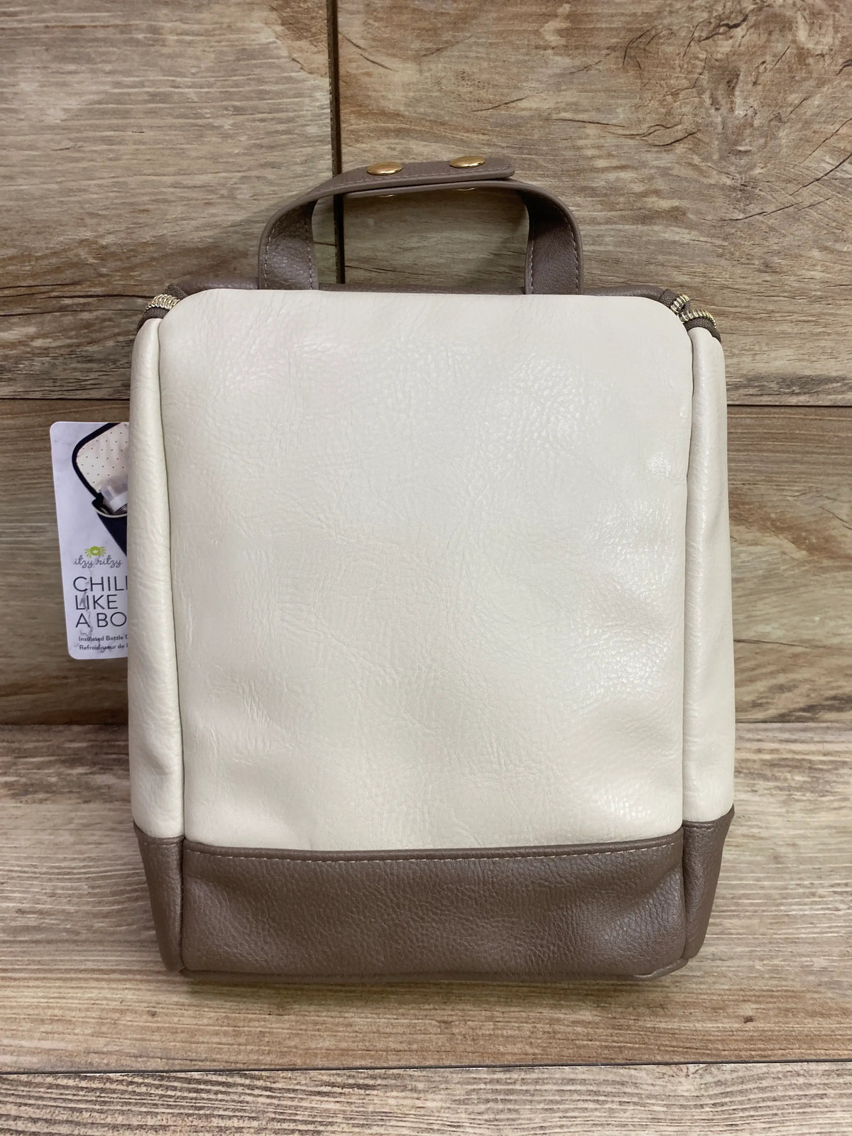 Front view of Itzy Ritzy insulated bottle bag in Vanilla Latte with cream and brown color blocking on wood grain