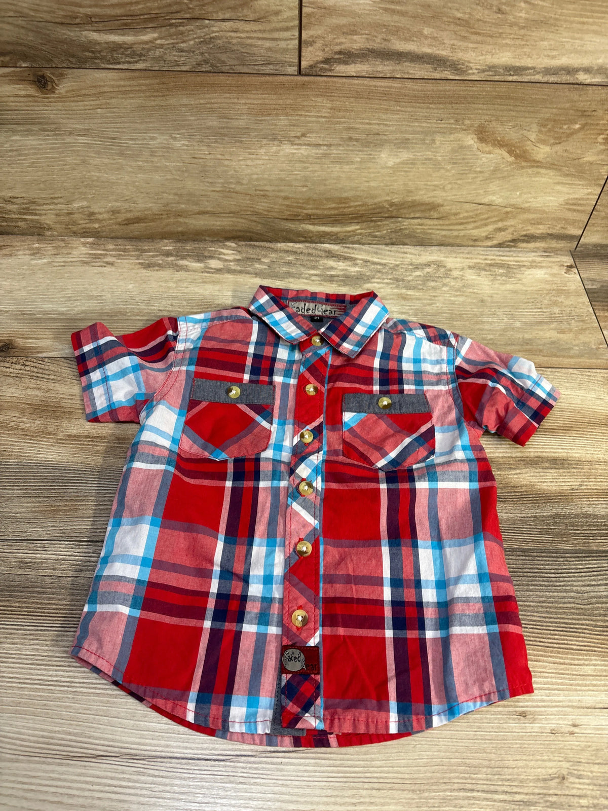 Front view of Faded Gear red plaid toddler button-up shirt with chest pockets and metal buttons on wood background