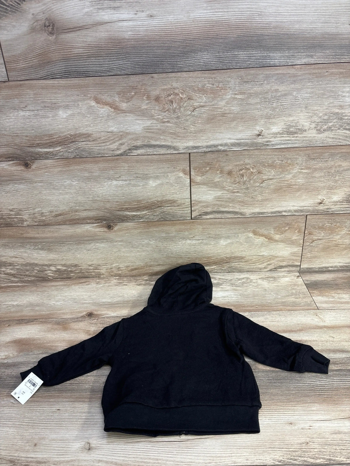 Black toddler hoodie with tag, laid flat on rustic wood floor background