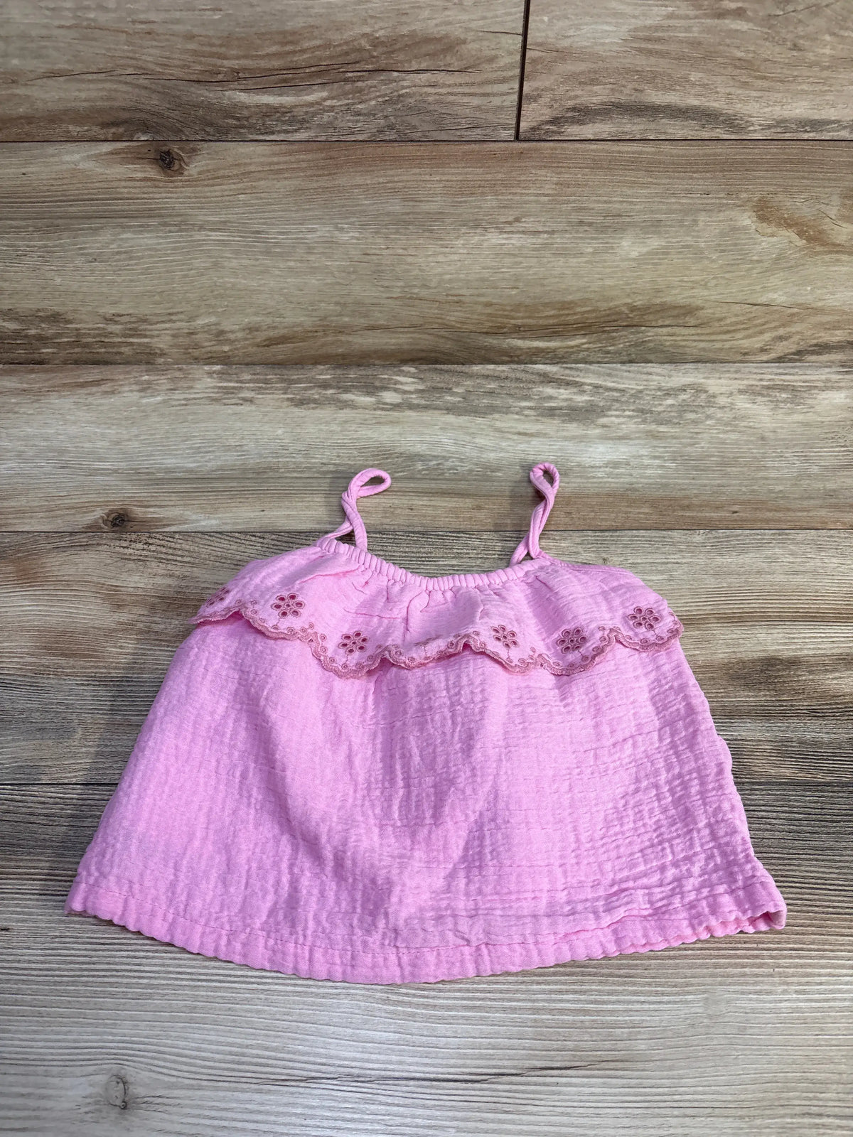 Flat lay of Gymboree pink eyelet gauze tank top, size 2T showcasing ruffled eyelet trim and looped spaghetti straps with light wood background