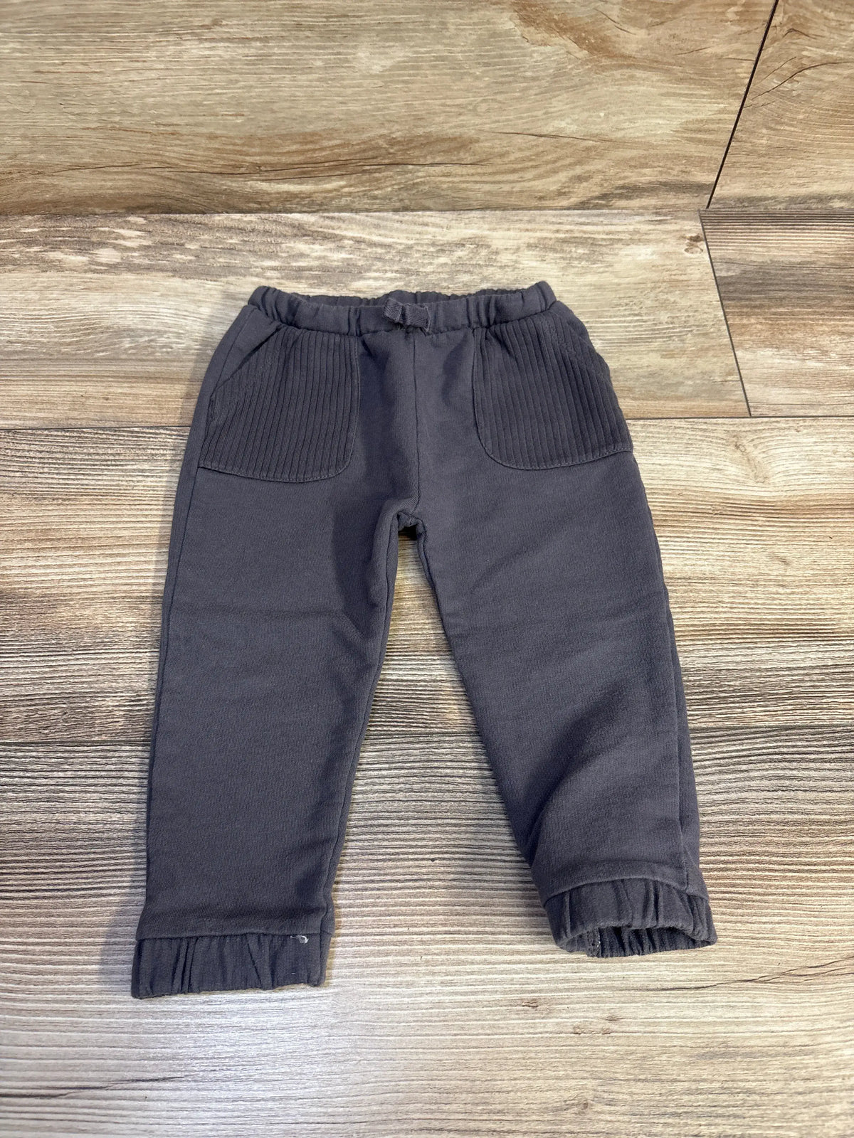 Grey Cat & Jack drawstring pants for size 12m infants on a wooden background.