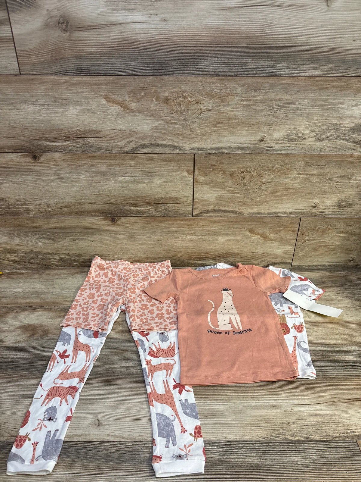 Four-piece toddler animal pajama set with rust shirt, leopard-print shorts, and white animal-print pants on a wood floor