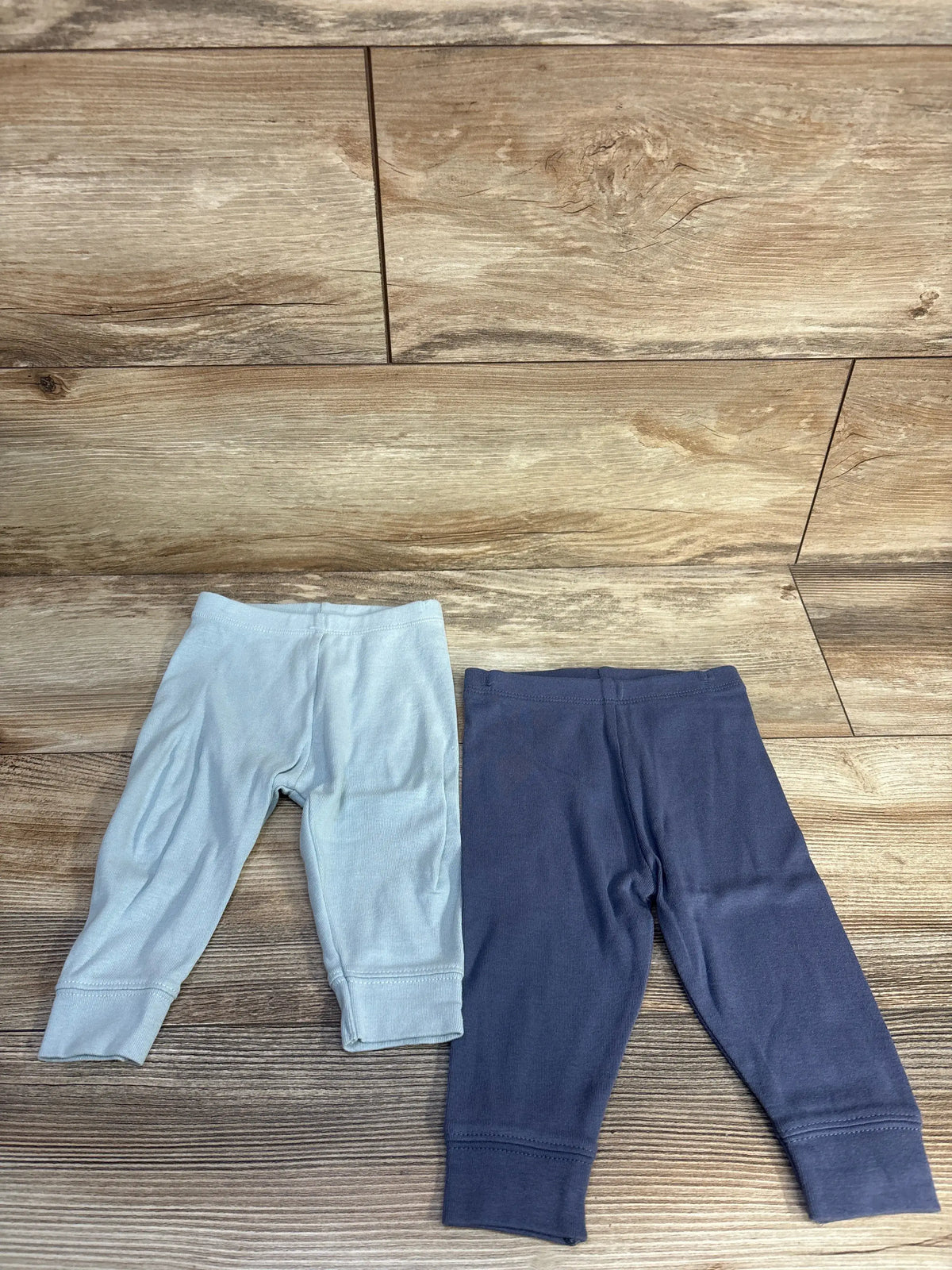 Two pairs of Cloud Island pull-on baby pants in light and dark blue on a wood background.