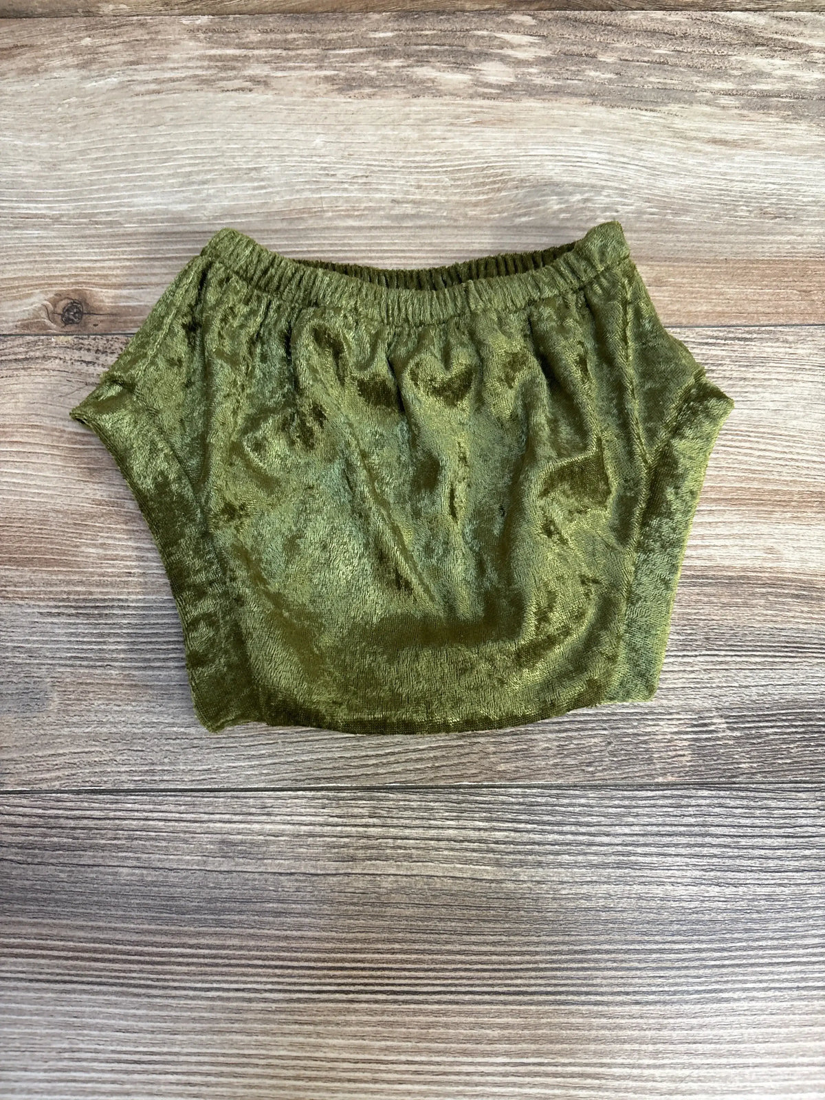 Top-down view of green velvet baby bloomers size 6-12 months showing elastic waistband and plush texture on wooden background