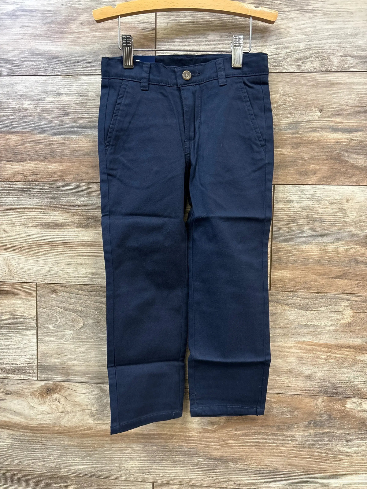 Front view of Izod flat-front toddler pants in navy showcasing front pockets and button closure with wood plank background