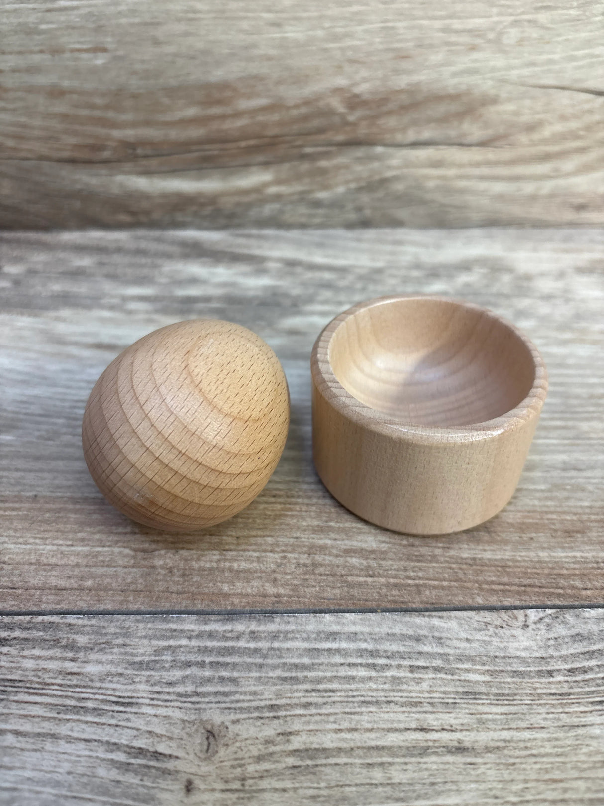 Light wood egg-shaped container with a removable hollow base on a wooden surface