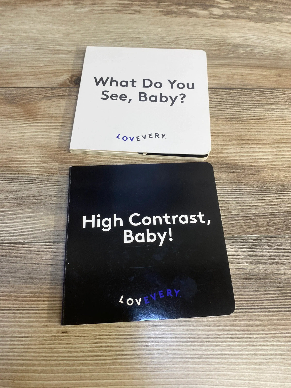 Two Lovevery baby board books on wood, titled 'What Do You See, Baby?' and 'High Contrast, Baby!'