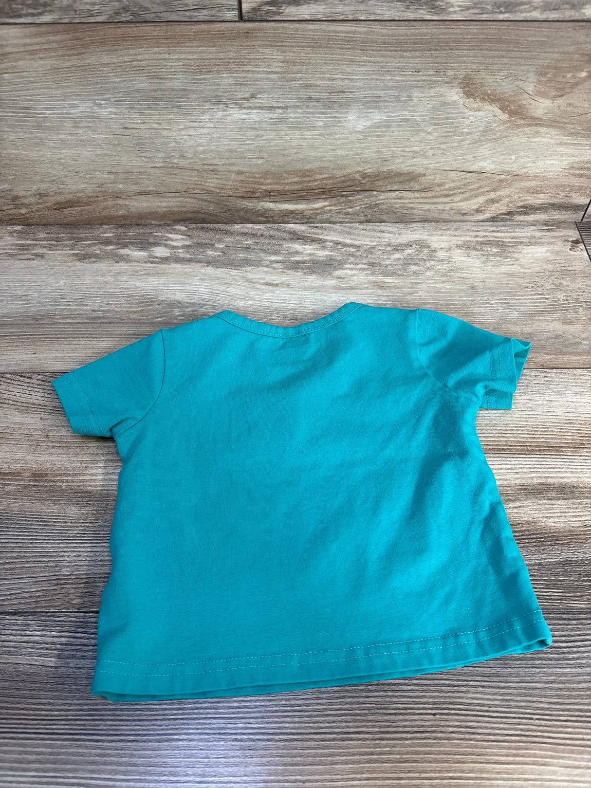 Back view of Caretoo 'Cooler Version of Dad' teal toddler t-shirt showing plain back and stitched hem, 12–18M, on wood floor