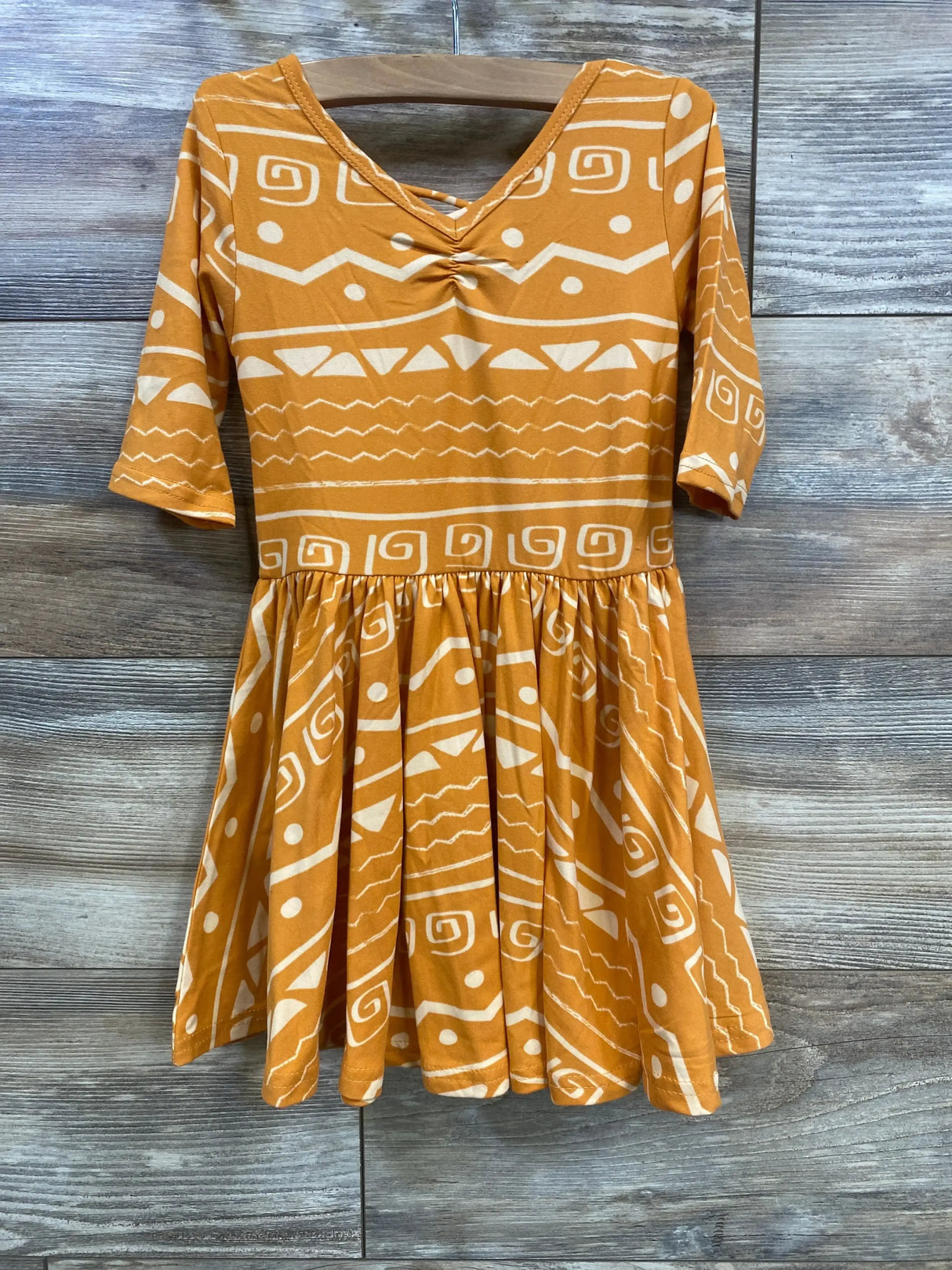 Front view of toddler orange patterned dress with gathered empire waist, elbow sleeves, and full skirt on wood background