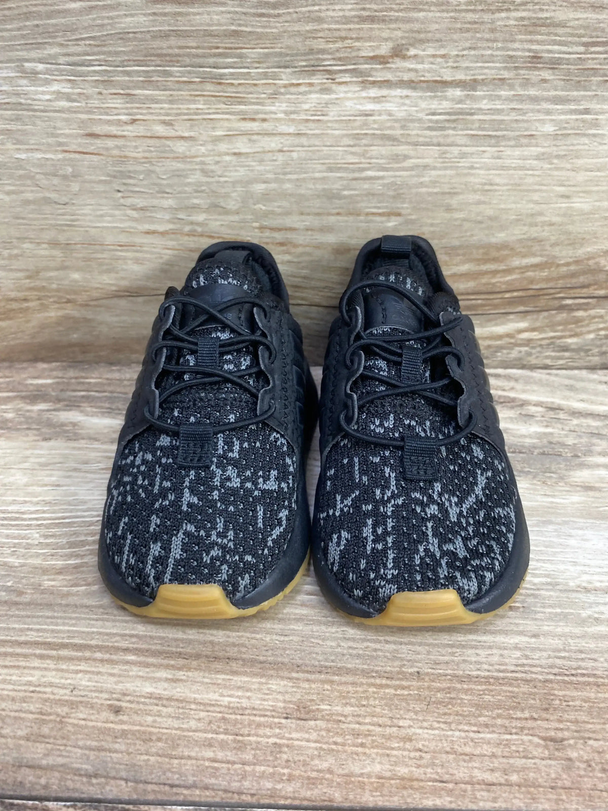 Black and gray patterned kids athletic sneakers with gum soles on wood background