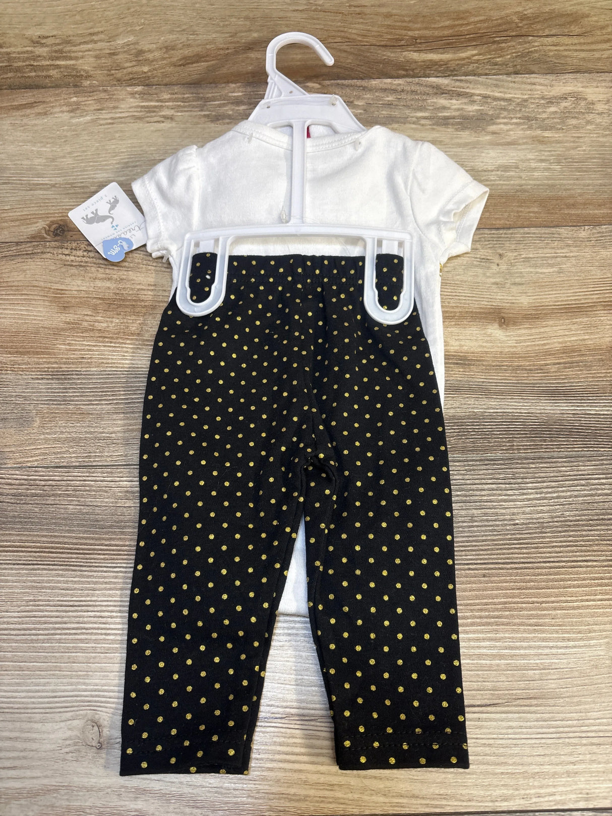 Flat-lay of newborn white short-sleeve bodysuit with black leggings featuring gold polka dots on wood background