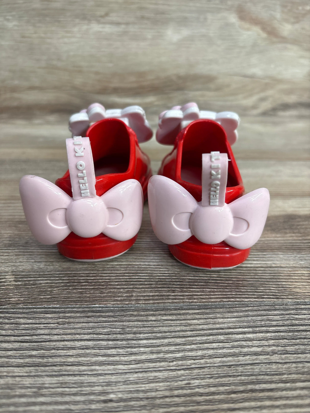 Red toddler shoes with pink bows and Hello Kitty text on wooden surface