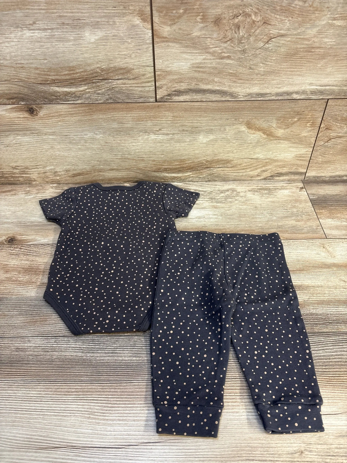 Back flat lay of grey baby bodysuit and matching pants showcasing small beige polka dots on dark grey fabric with wood plank floor background