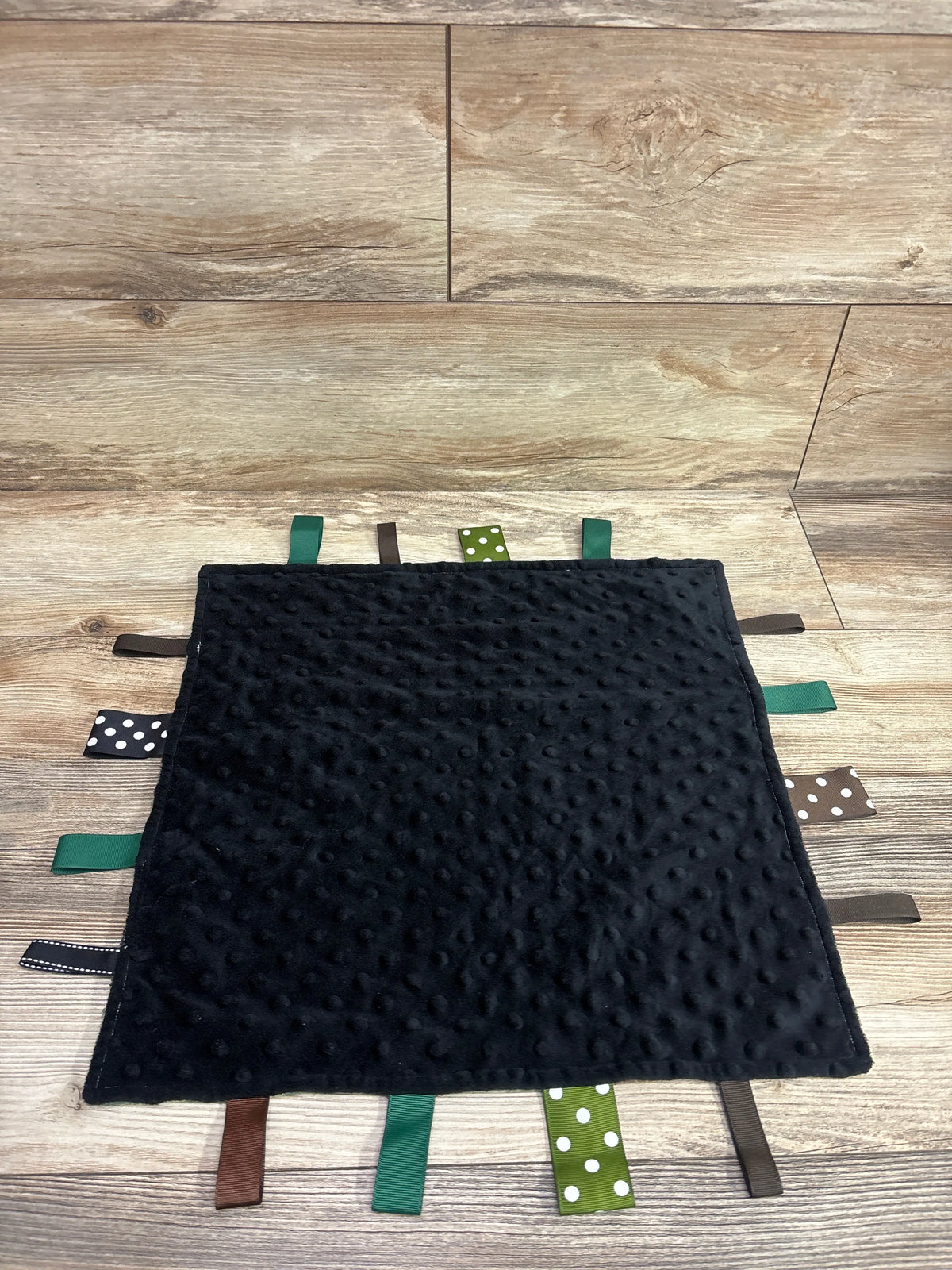 Front view of FOMAISELF black minky dot and camo tag ribbon baby blanket showcasing textured dots and colorful ribbons on wood flooring