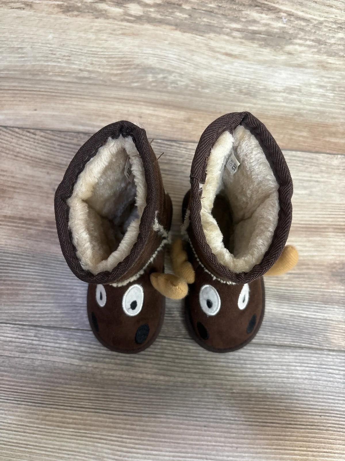 Top-down view of Lazy One Kid's Moose slipper boots showcasing plush faux fur lining and embroidered moose faces on wood floor