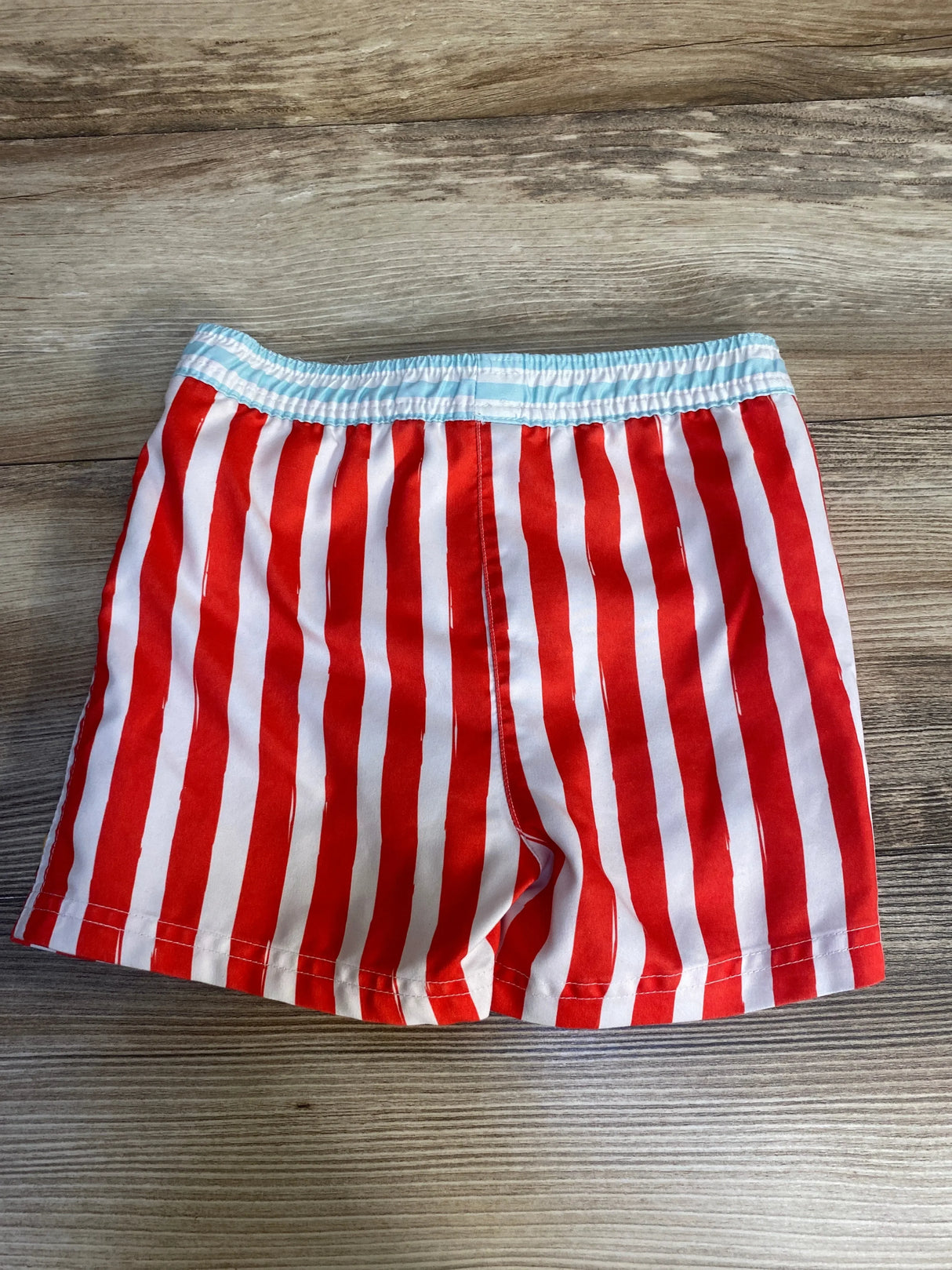 Back view of Mickey Mouse swim trunks showcasing red and white vertical stripes and elastic waistband with light blue trim on wood background