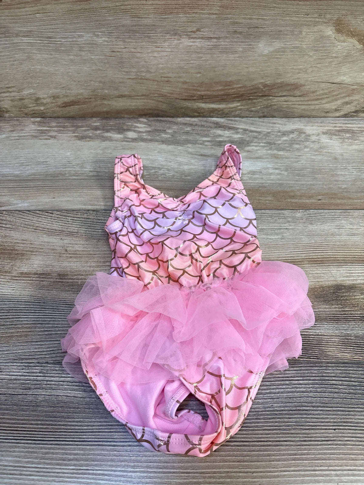 Top down view of toddler pink mermaid one-piece swimsuit with gold scale print and pink tulle tutu on wood background