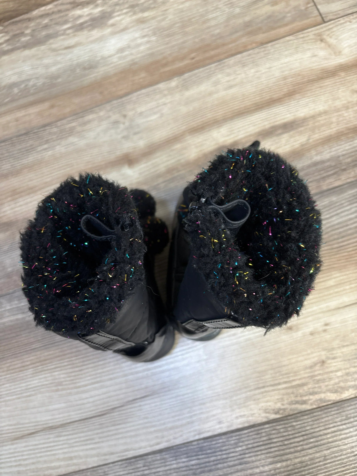Black kids winter boots with fuzzy, multicolor sparkle trim on wood floor
