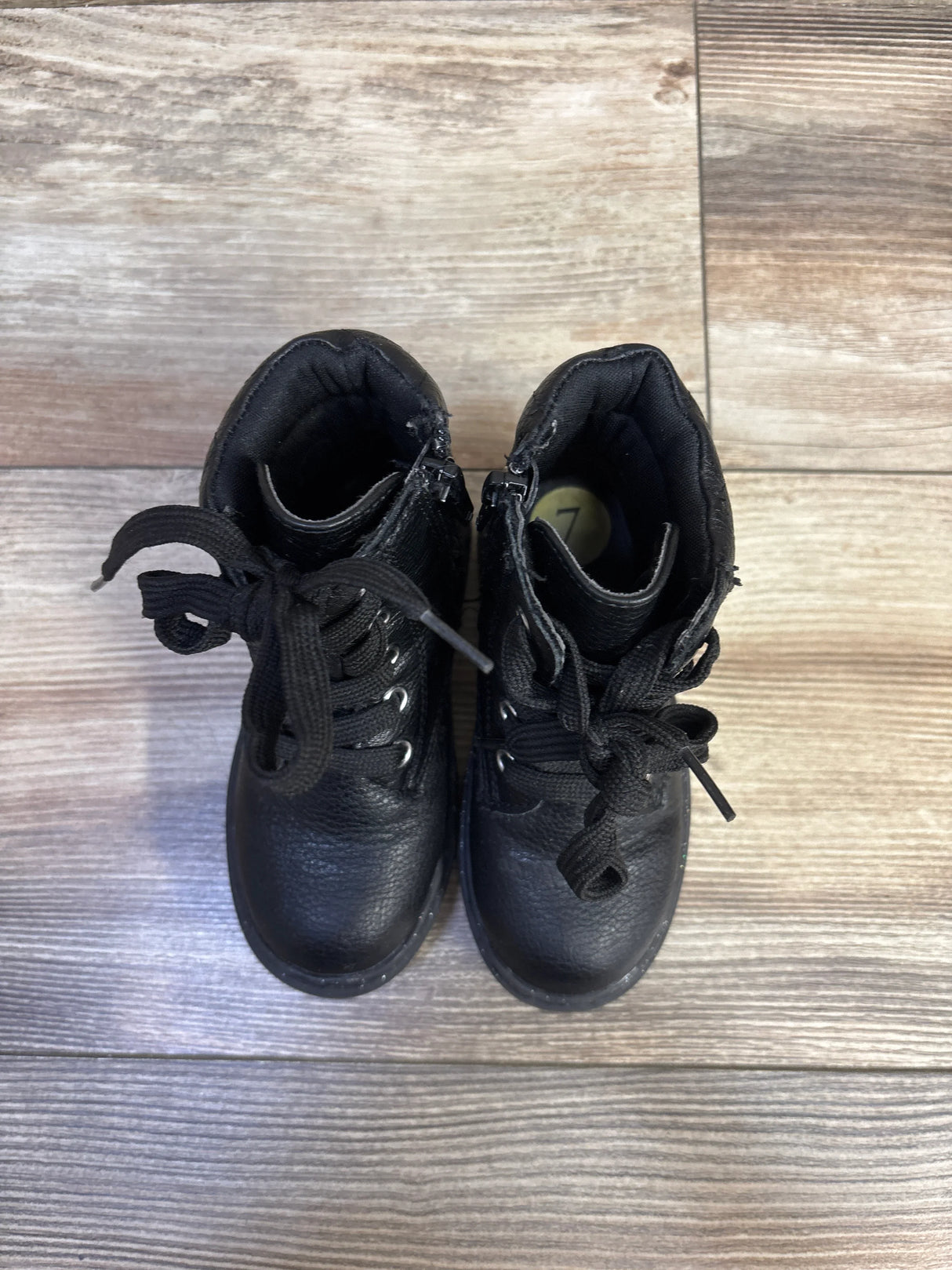 Top view of Sincerely Jules black glitter lace-up boots showing laces, side zippers, and size 7C insole on wood floor
