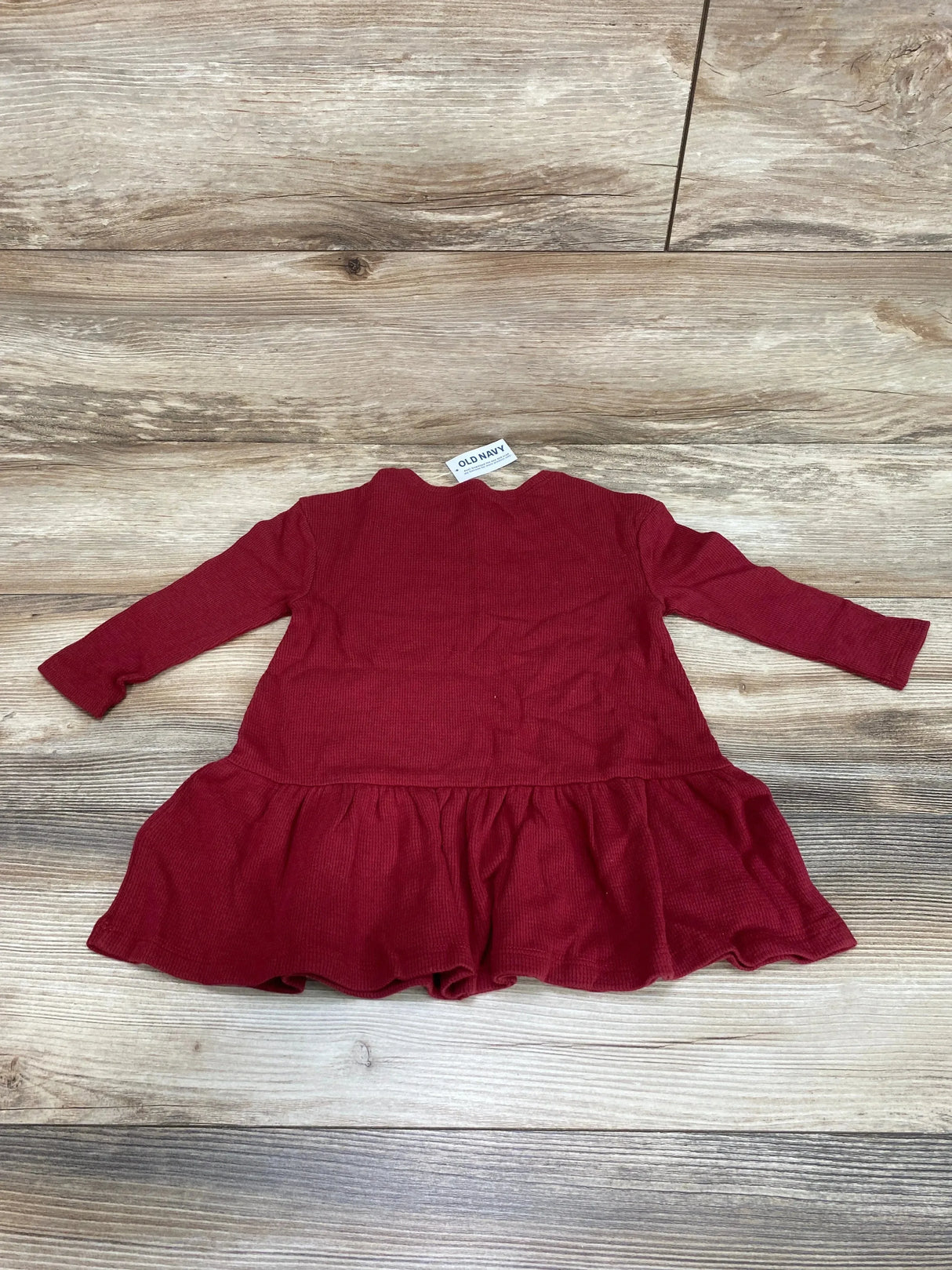 Flat lay of Old Navy crimson peplum thermal toddler dress showing back view and long sleeves on wood floor size 18 to 24 months