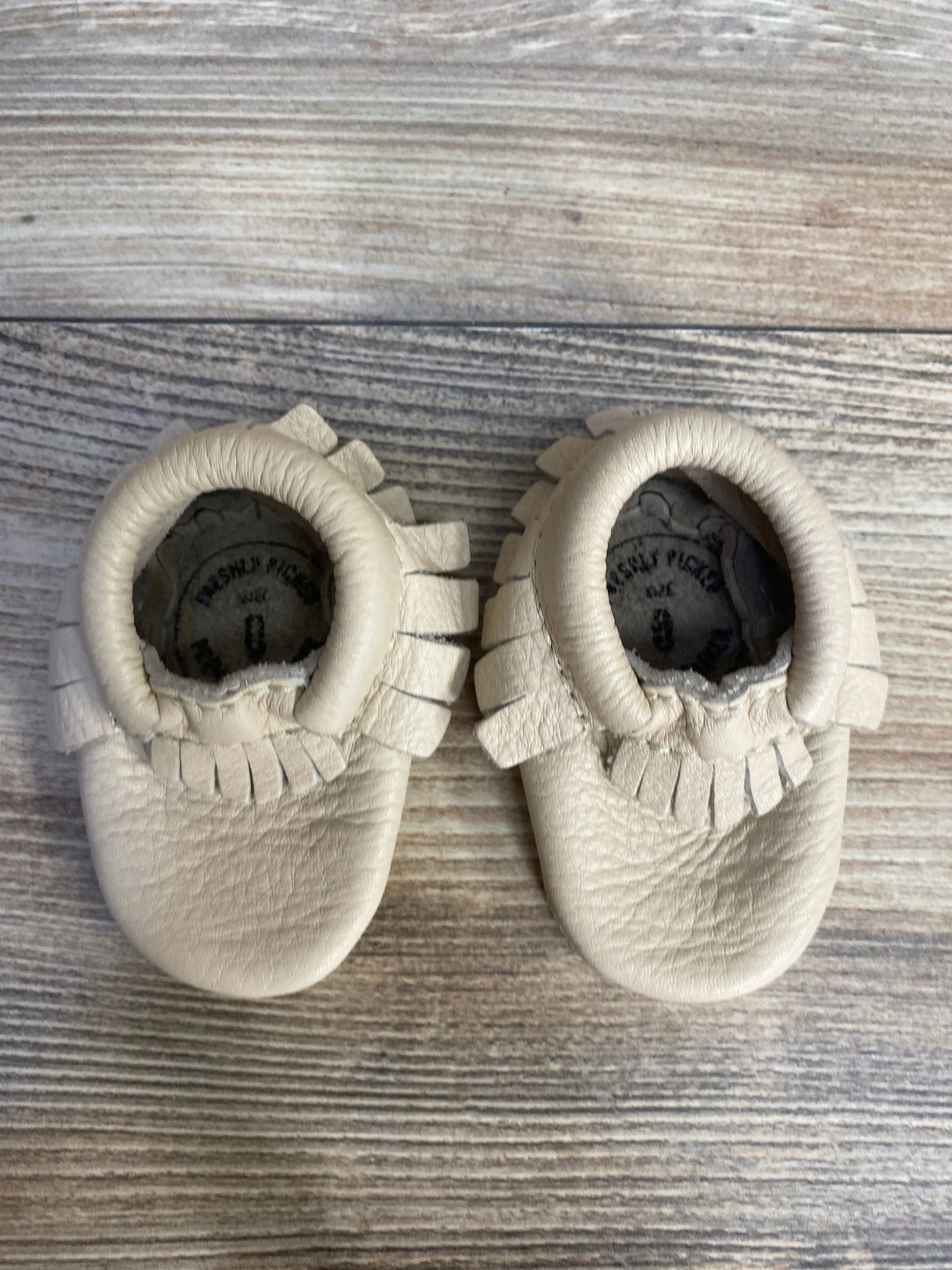 Beige leather baby moccasins with fringe detail on wood background