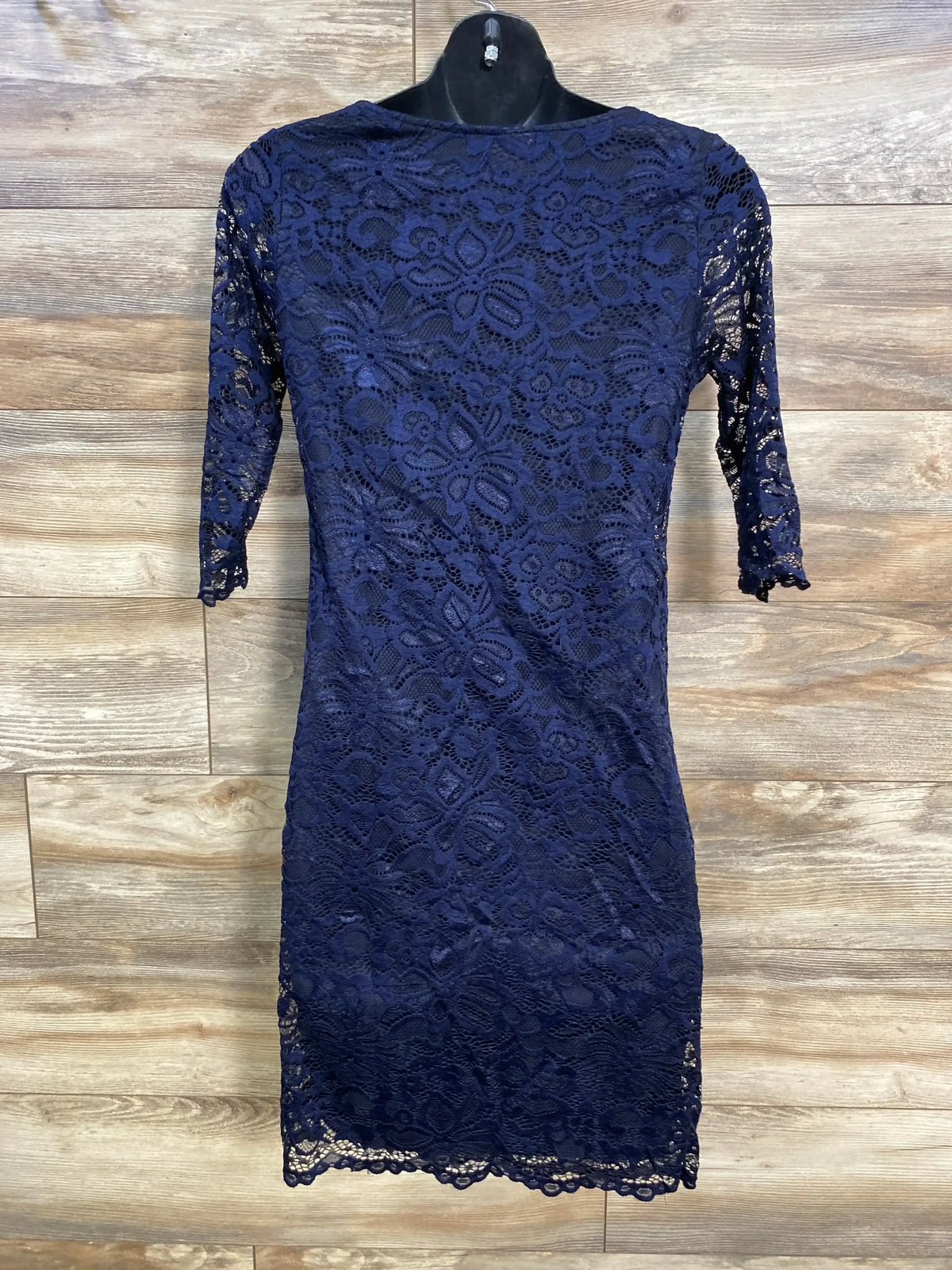 Front view of Pink Blush navy maternity fitted lace dress with three-quarter sleeves on a hanger against wood background