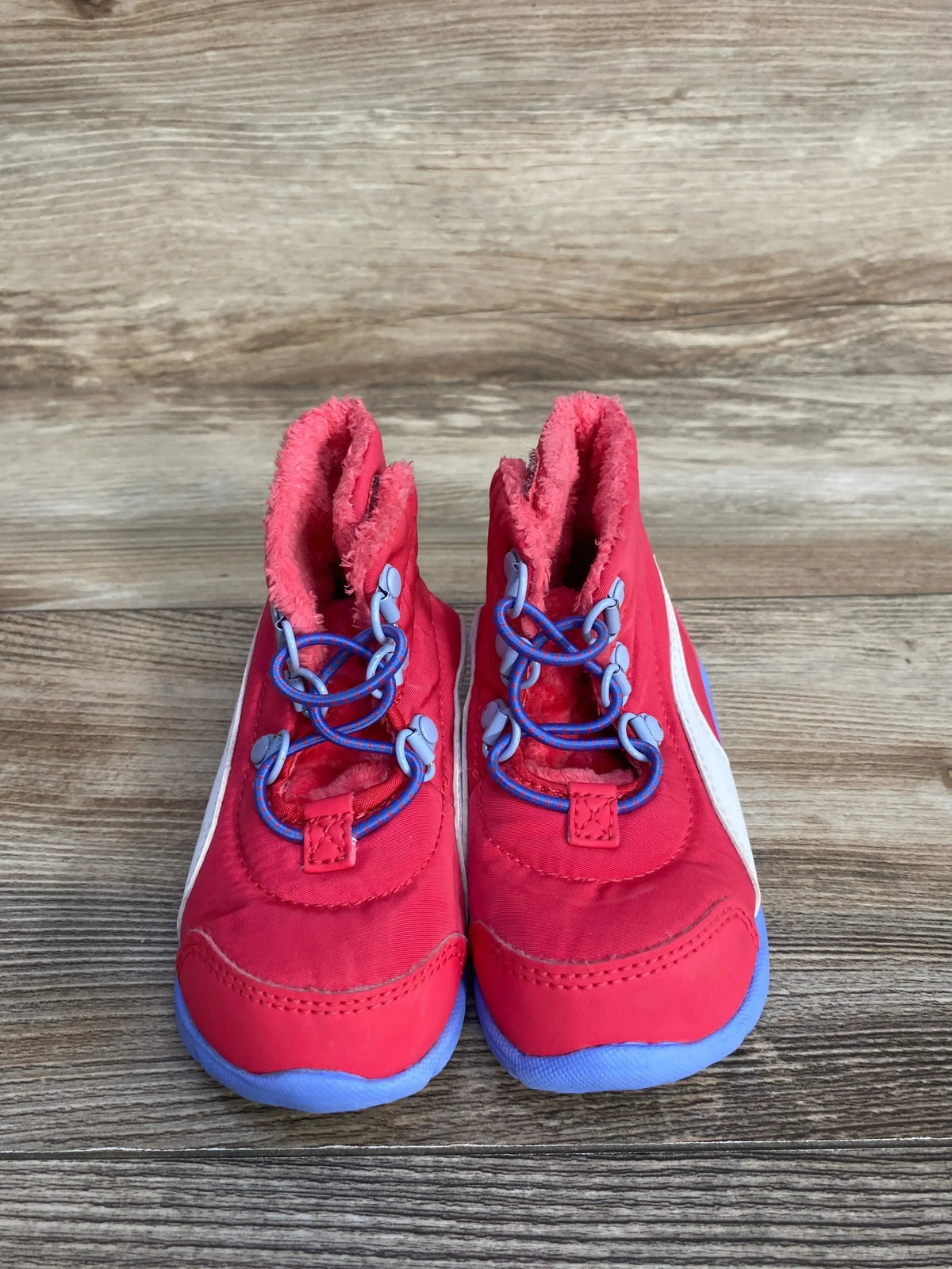 Front view of Puma Bao 3 AC toddler snow boots showcasing blue soles, purple bungee laces, faux-fur lining and white side stripe with wooden floor background