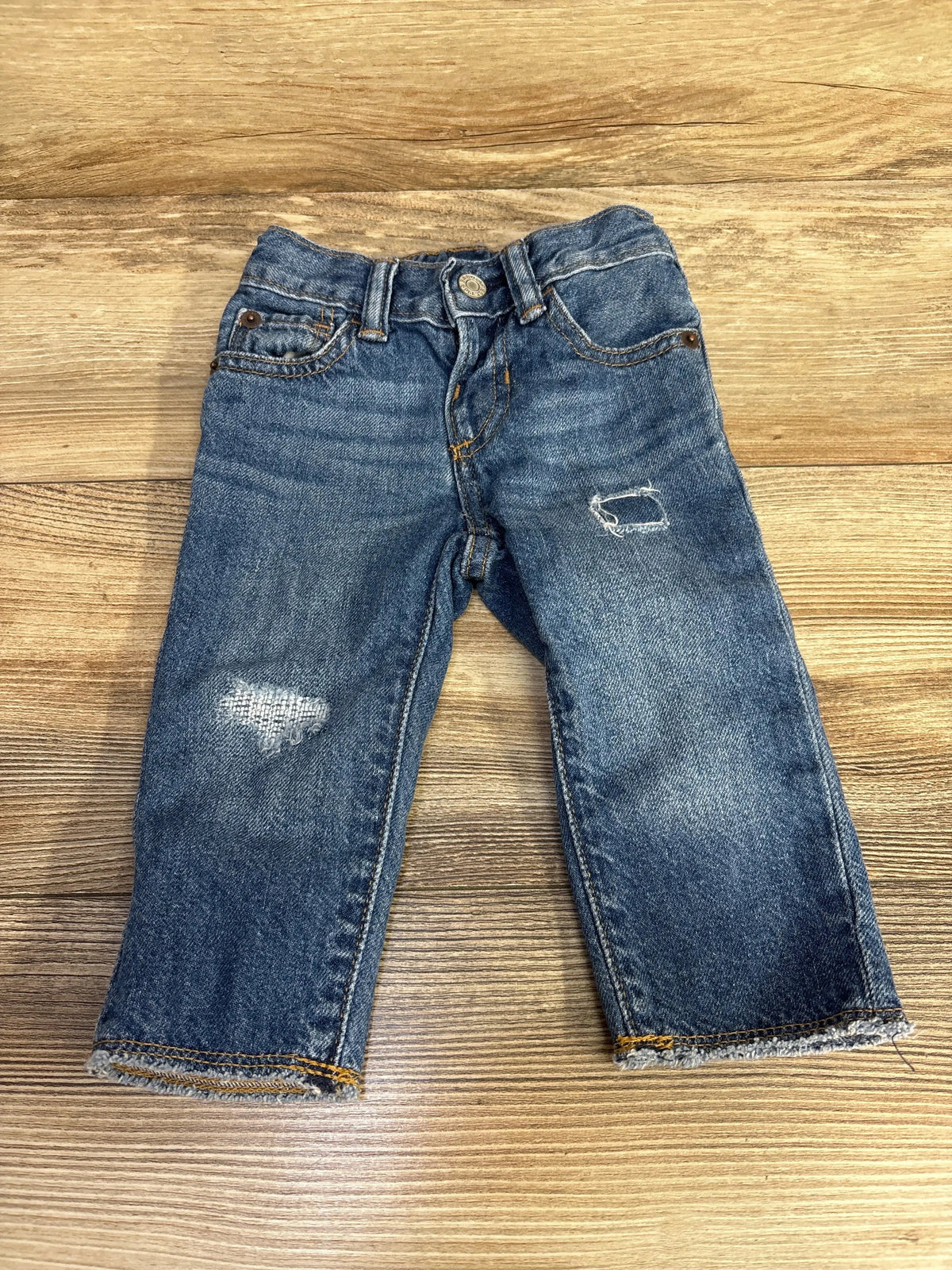 Front flat lay of Gap slim toddler denim jeans size 6 to 12 months showing distressed knee patches and frayed hems on wood background