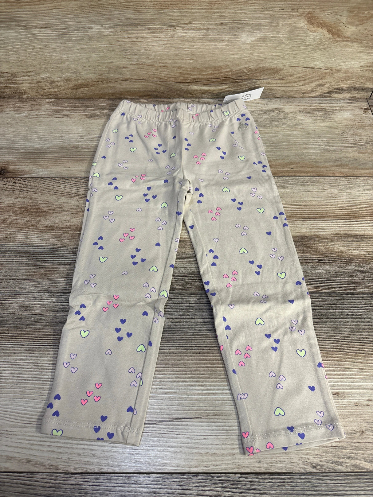 Beige toddler pants with pastel heart print on wood background