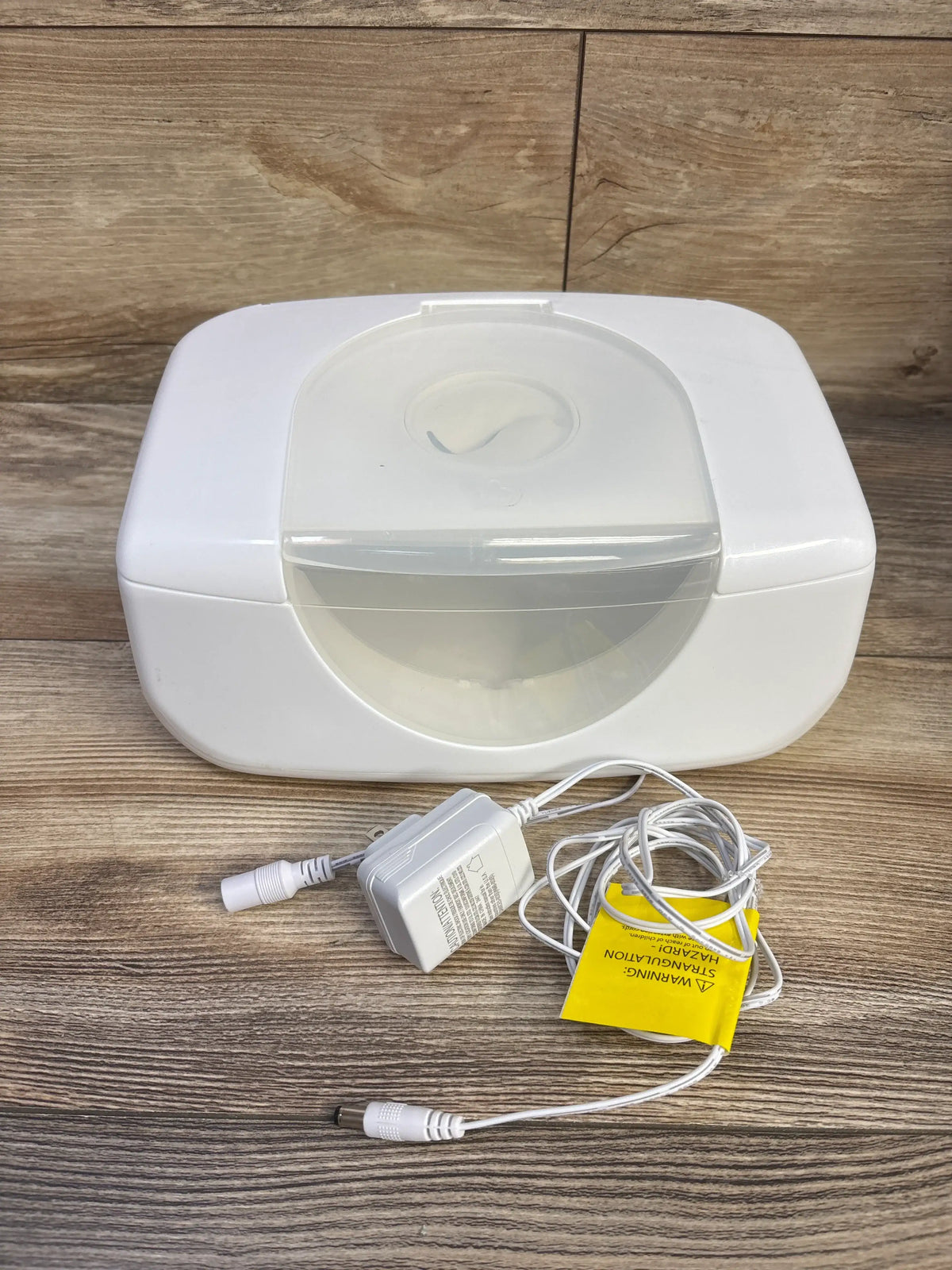 Front view of white Munchkin Bright & Warm wipe warmer with translucent lid and power adapter on wood-look surface