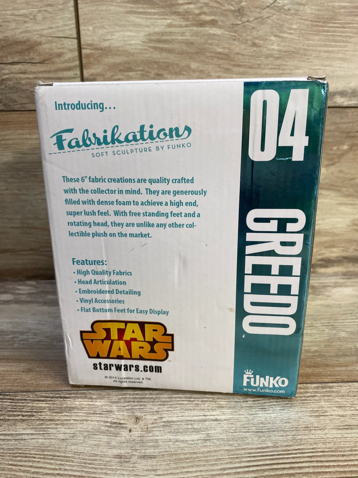 Front of boxed Funko Fabrikations Greedo plush showing packaging with large 04, Star Wars and Fabrikations logos on floor