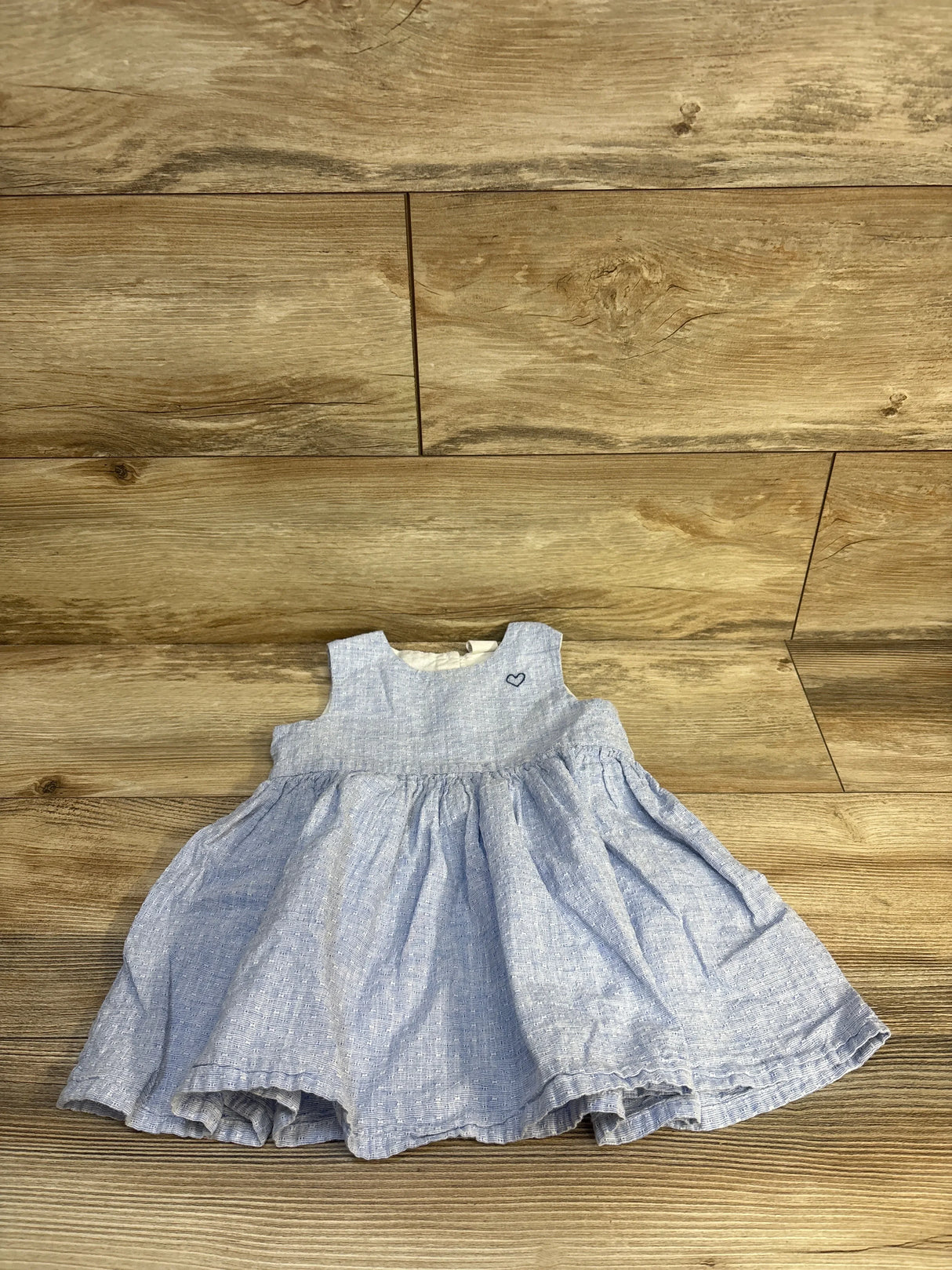Flat lay of H&M blue linen-blend baby dress with sleeveless bodice, gathered skirt, and embroidered heart on wood background