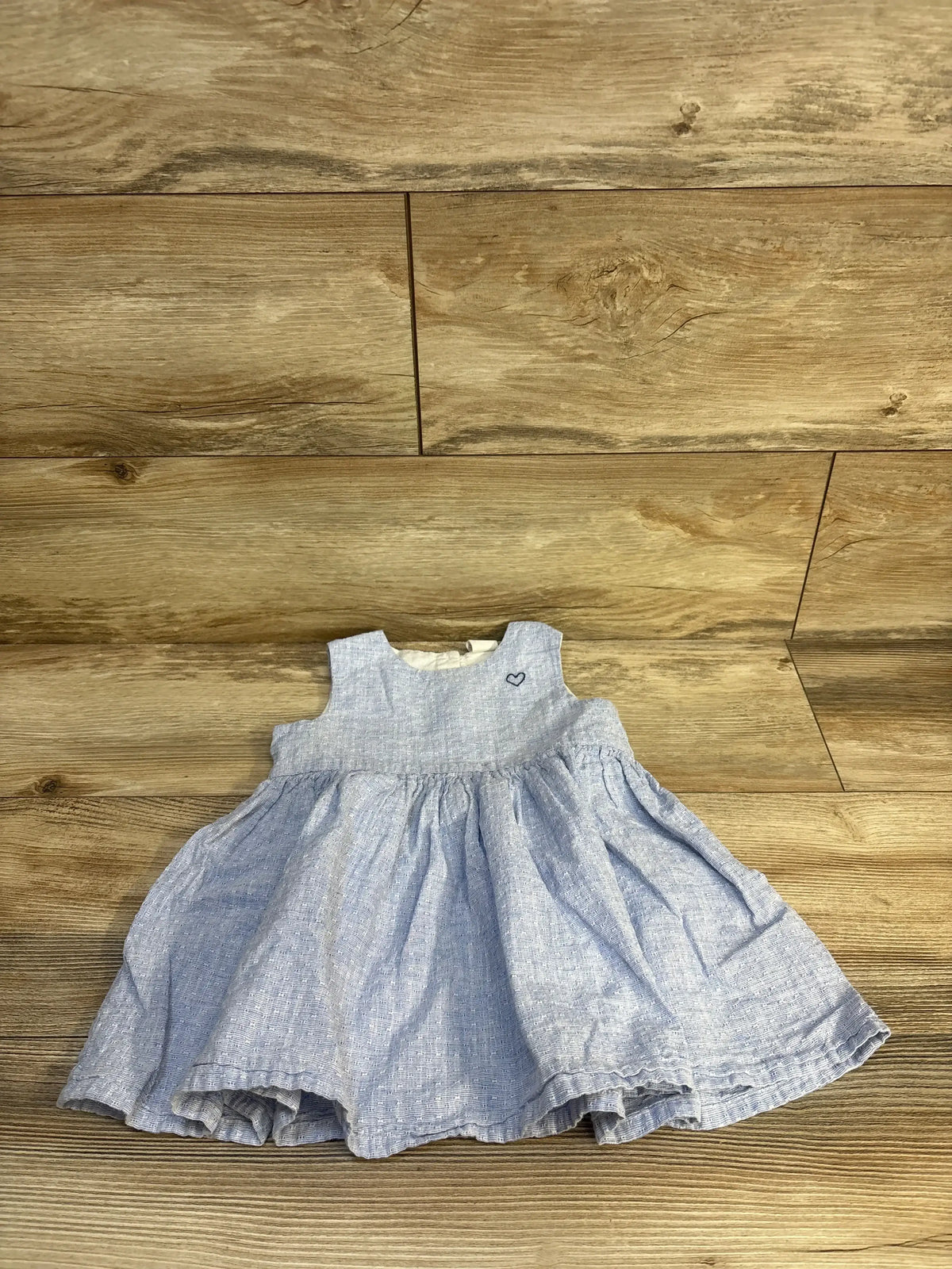 Flat lay of H&M blue linen-blend baby dress with sleeveless bodice, gathered skirt, and embroidered heart on wood background