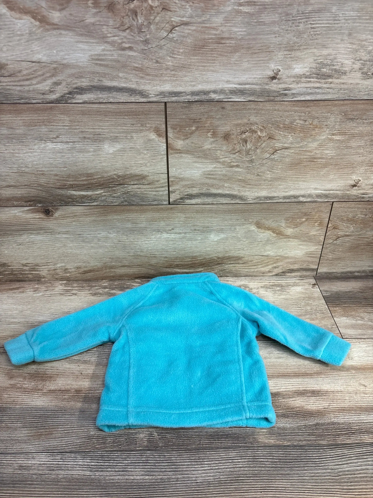 Back view of Columbia teal fleece full-zip jacket size 3-6 months showing soft fleece texture and raglan sleeves on wood floor
