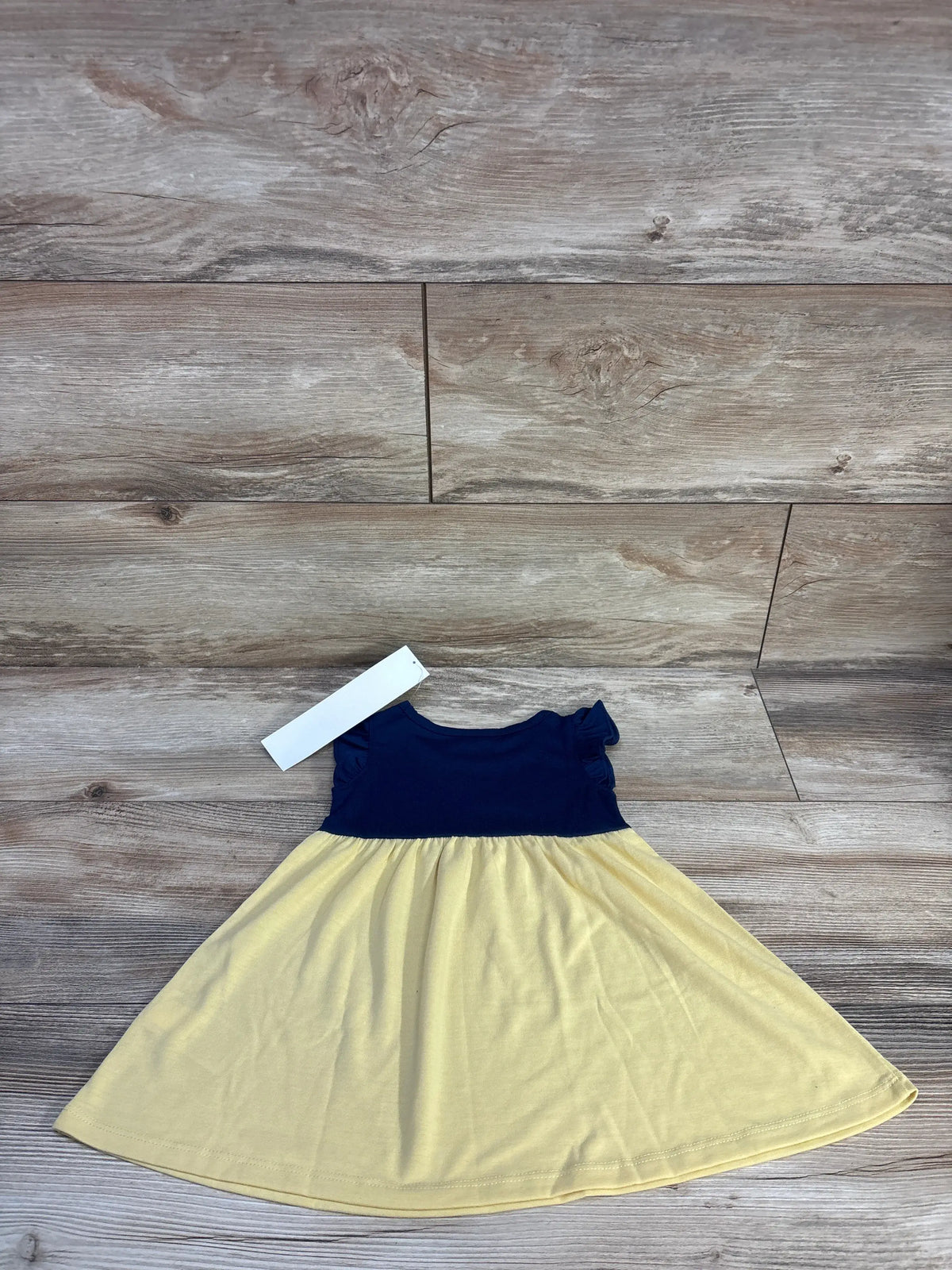 Front view of Baby Gap x Disney Snow White PJ dress showcasing navy bodice, yellow skirt, and flutter sleeves on wood flooring