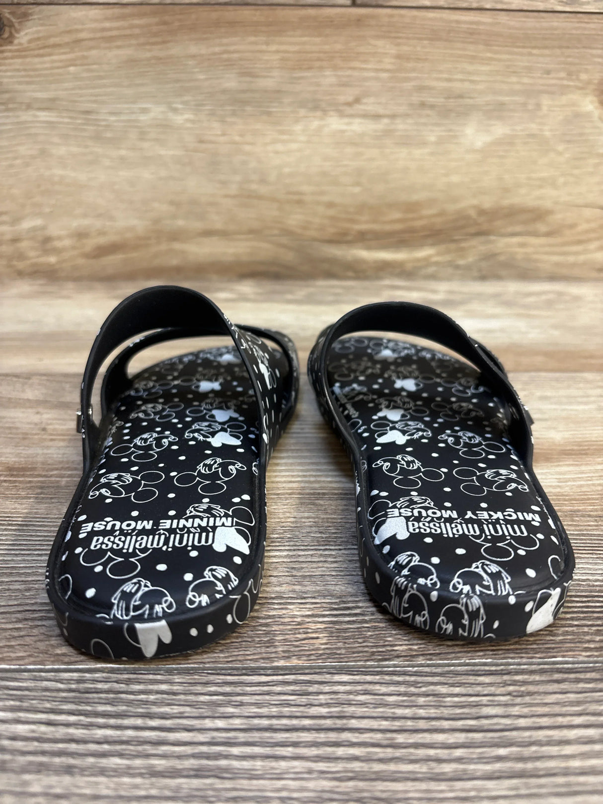 Top view of mini Melissa Minnie and Mickey Mouse jelly sandals in black and white print on wood plank floor