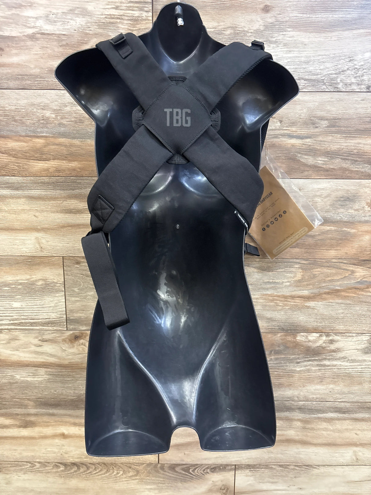 Top-down view of Tactical Baby Gear carrier showing padded X-back straps and TBG logo on wood floor