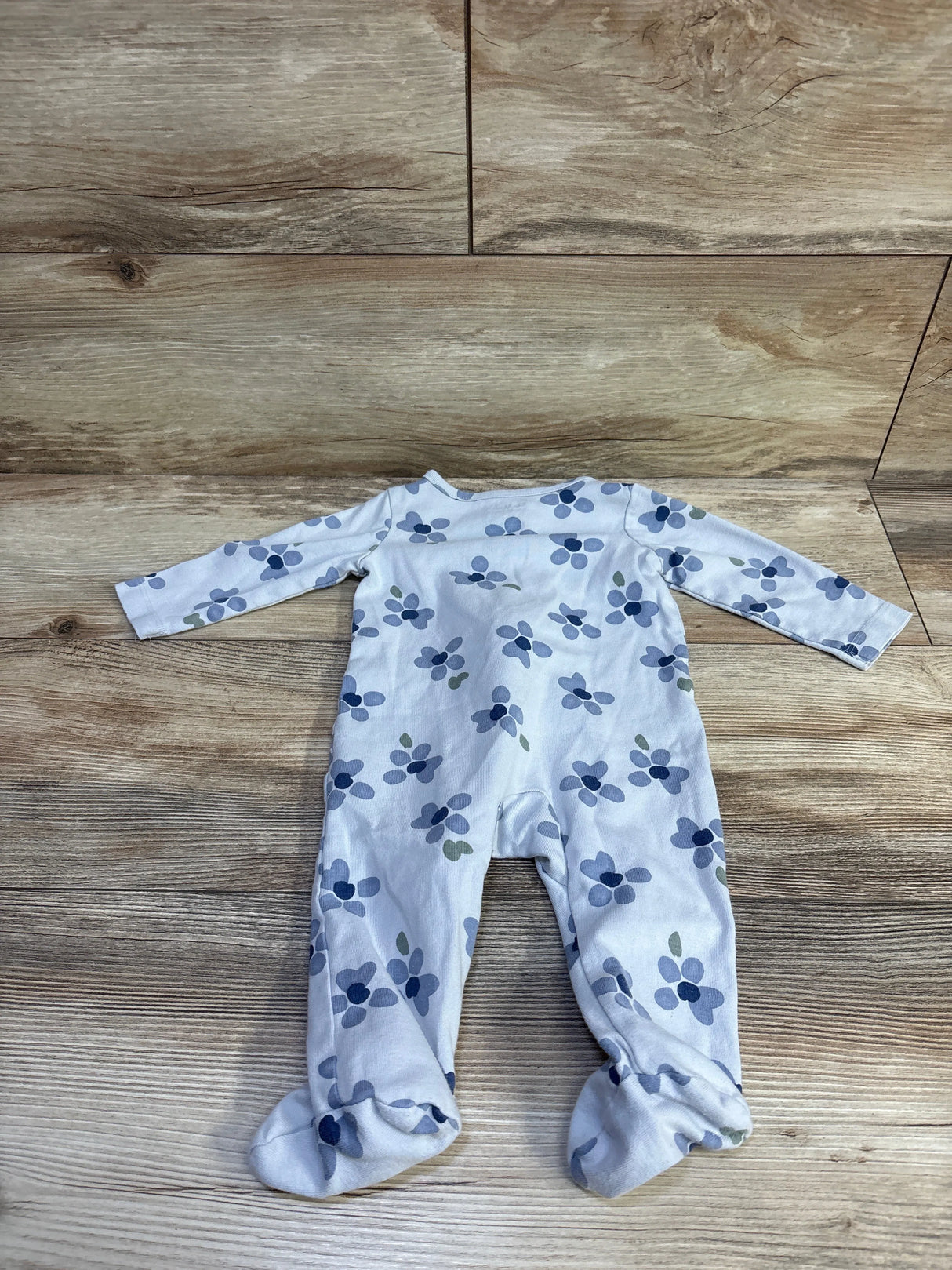 Flat lay of blue floral footed baby sleeper showing long sleeves and enclosed feet on wood background