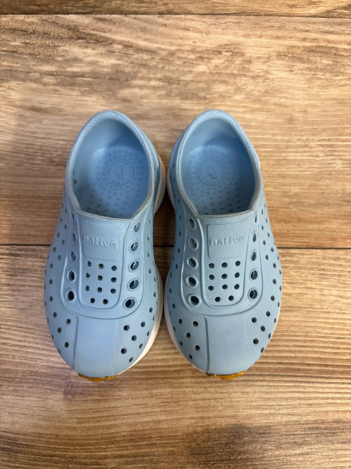 Pair of blue Native Robbie Sugarlite slip-on shoes for kids, size 6c, on a wood surface.