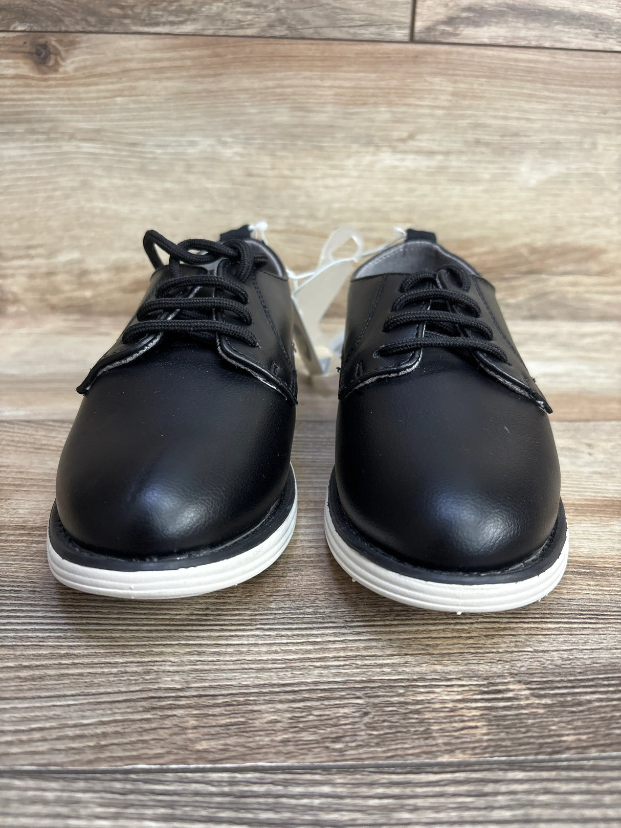 Front view of Cat and Jack Alfi dress shoes size 13c showcasing black faux leather upper with black laces and white sole on wood plank floor