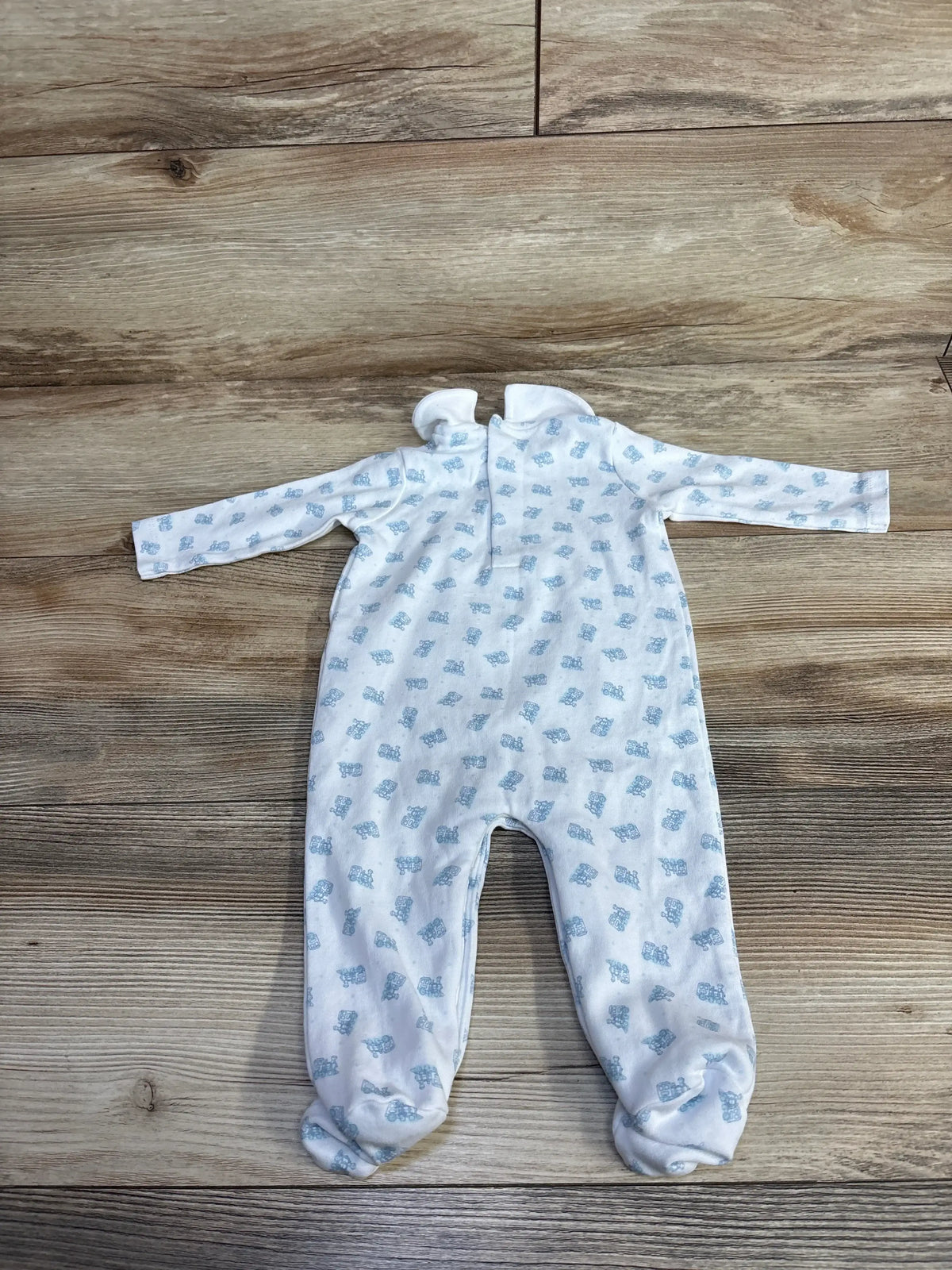 Flat lay of Edgehill Collection white train footie (3M) with long sleeves, footed legs, and blue train print on wood floor