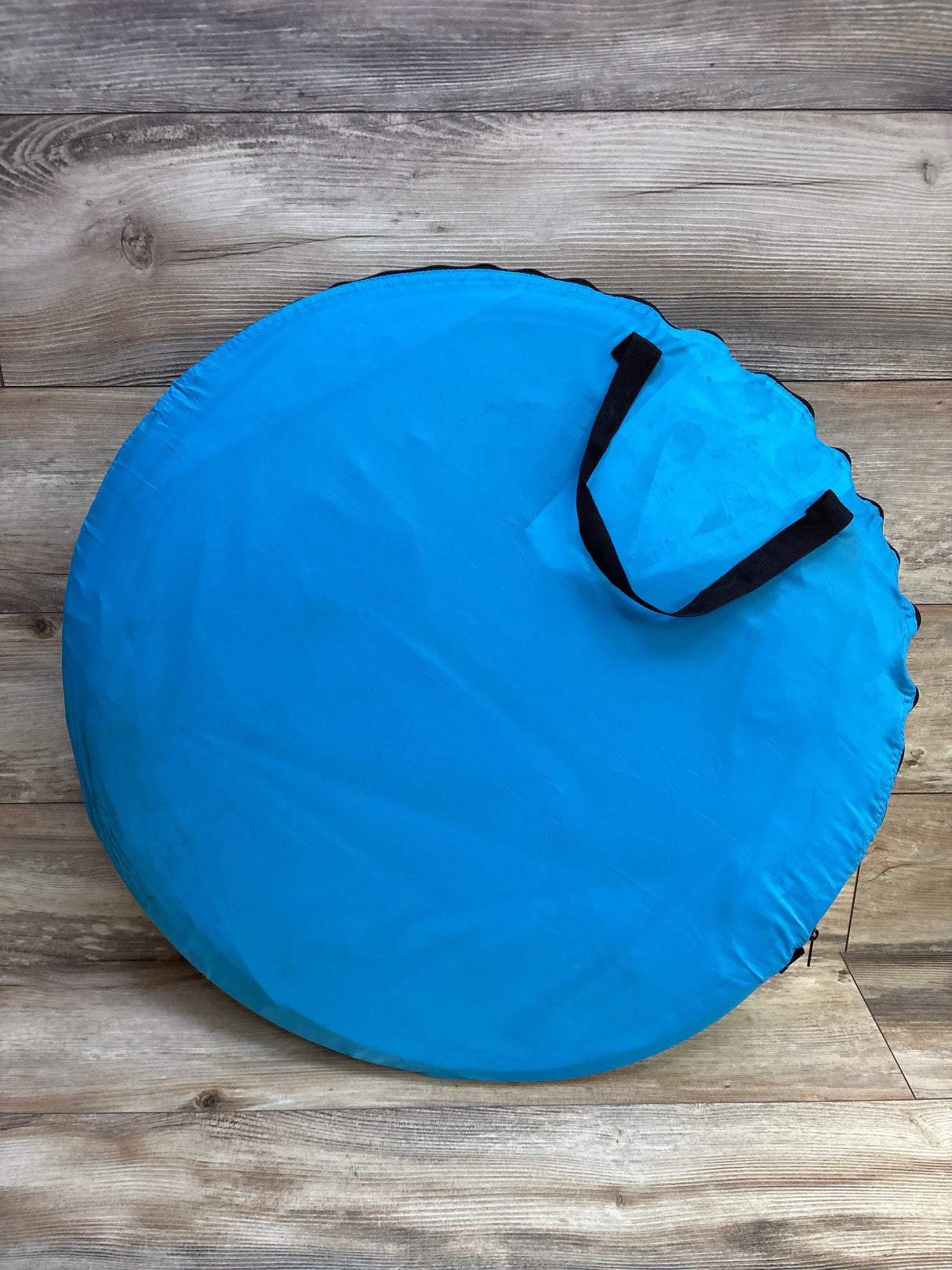 Blue round zippered carrying case with black handles on a wooden floor
