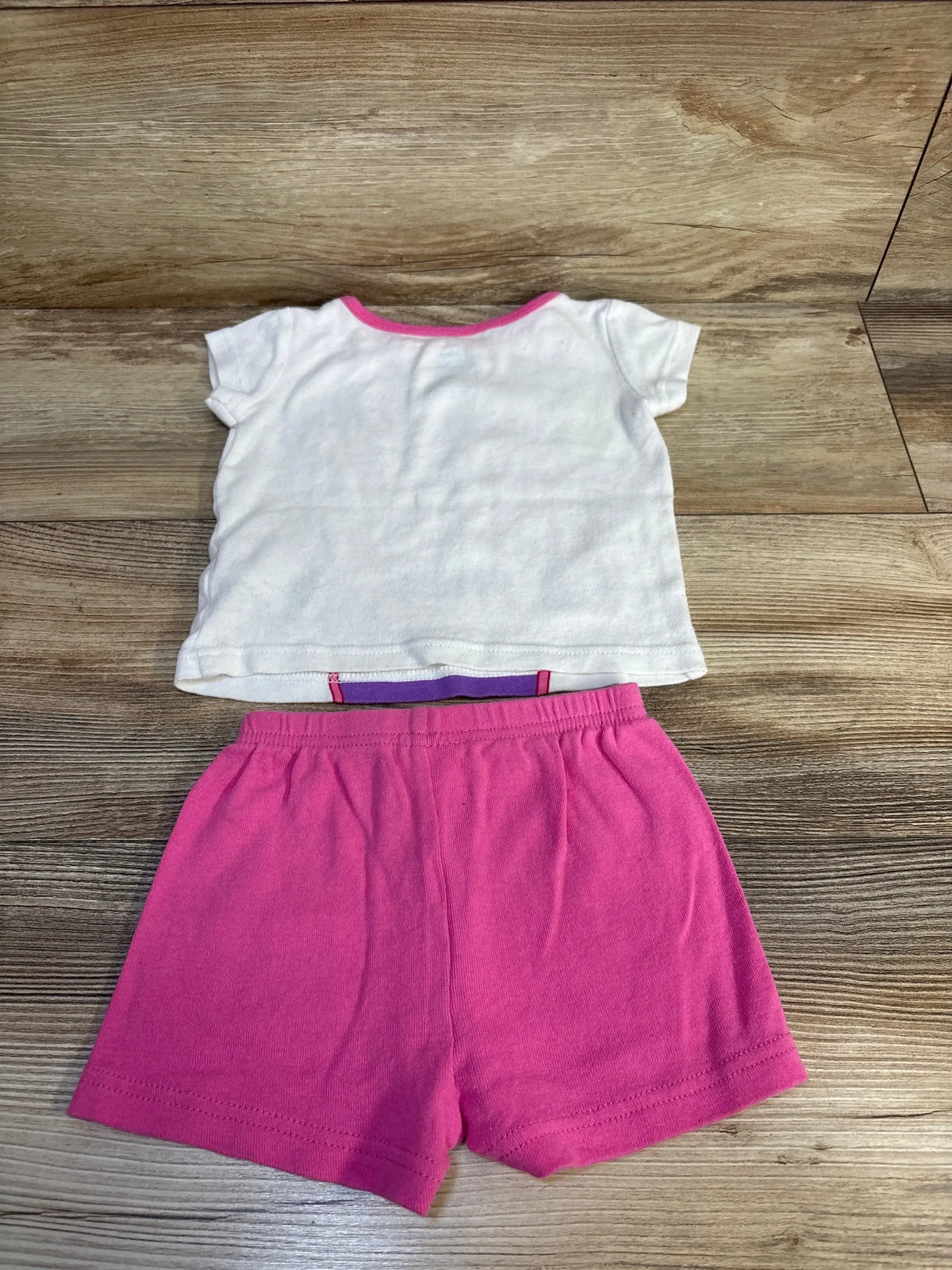 Back view flat lay of girls white short sleeve tee with pink trim paired with pink shorts on wood plank floor