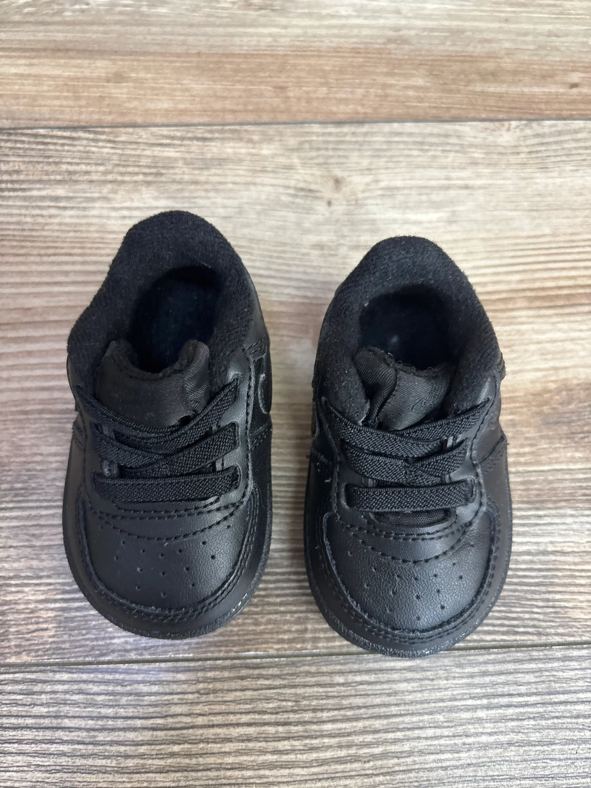 Pair of black infant sneakers with laces on wooden floor, children's resale footwear