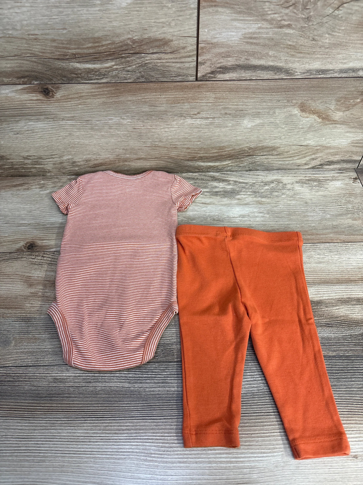 Striped baby onesie and orange leggings set on wood background