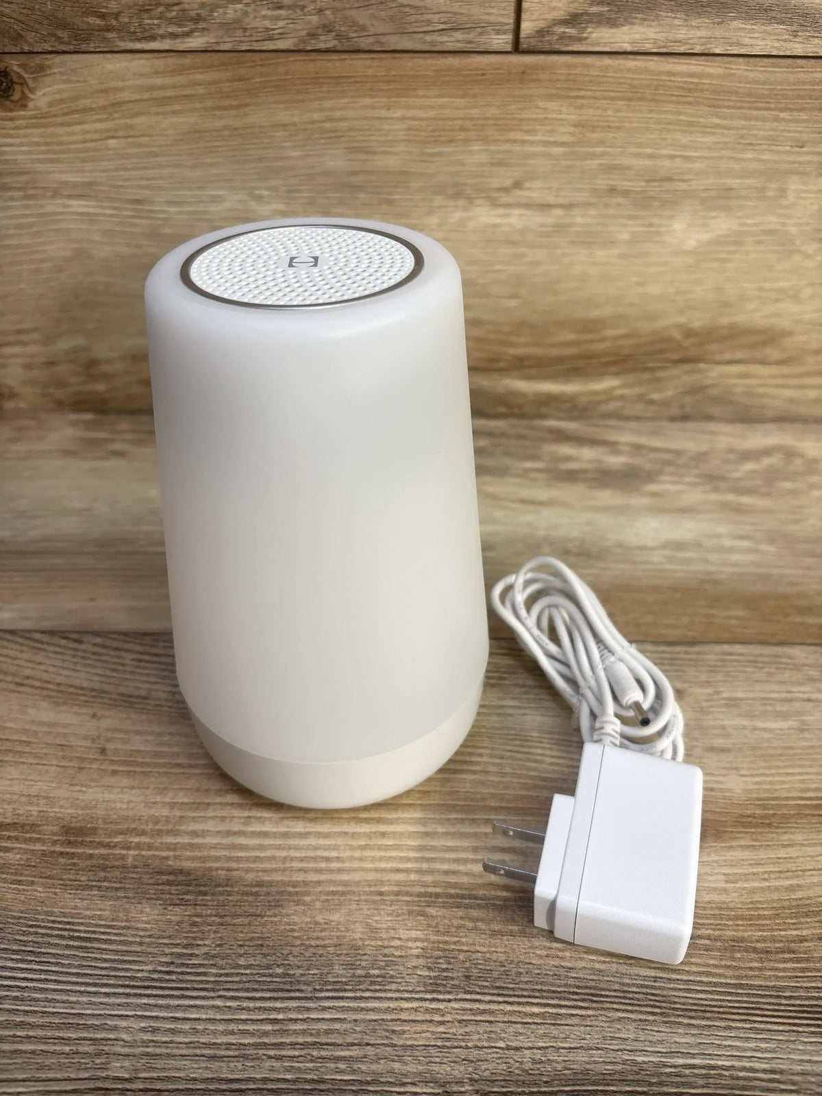 Front view of a white cylindrical electronic device with power adapter on a wood surface