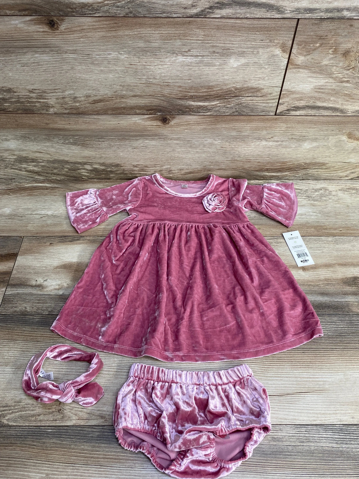 Pink velvet baby dress set with matching bloomers and headband on wooden background