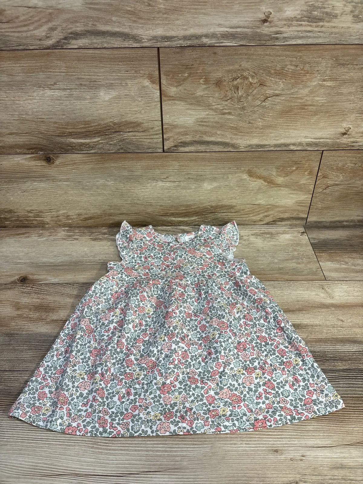 Flat lay of H&M white cotton baby dress, 18 months, showing pink-green floral print and flutter sleeves on wood floor